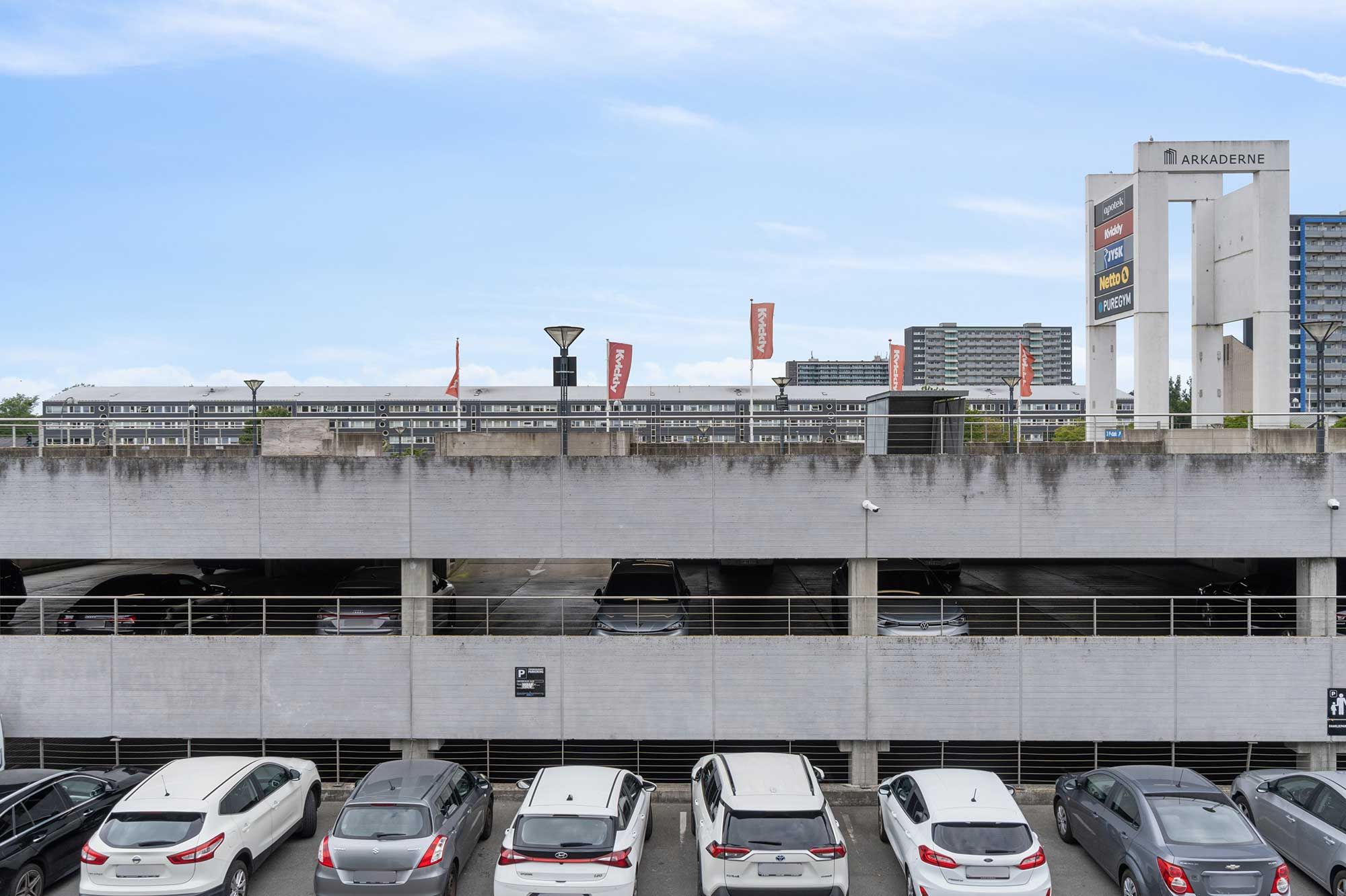 Lejlighedsbygning med garage, parkeringspladser, kontorer og faciliteter. Arkaden med skilte og røde flag. Moderne bygningsstruktur med flere højhus.