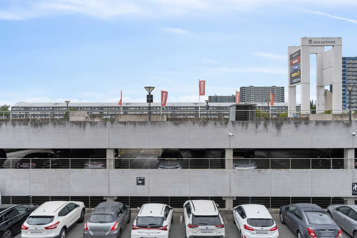 Lejlighedsbygning med garage, parkeringspladser, kontorer og faciliteter. Arkaden med skilte og røde flag. Moderne bygningsstruktur med flere højhus.