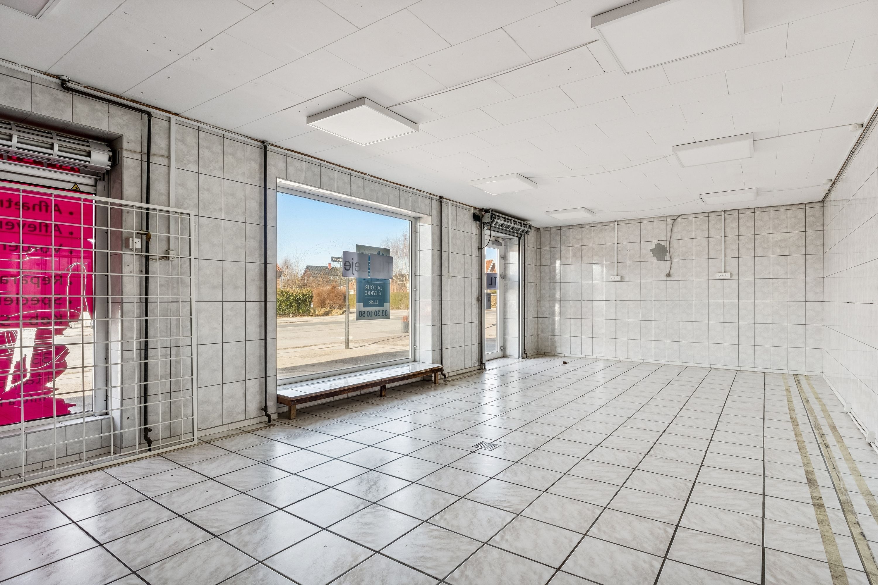 Store butikslokaler til leje i Gentofte med højt loft, vinduer og en glasdør. Indvendigt er lokalet tomt med blanke vægge og gulv.