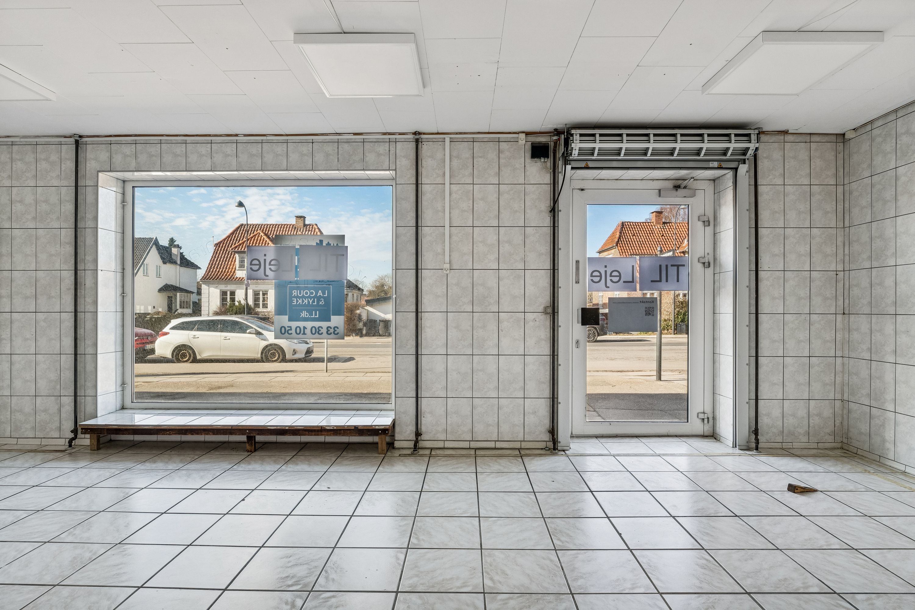 Lejemål i Gentofte med tilhørende parkeringsplads og adgangsdør til en butik med store vinduer.