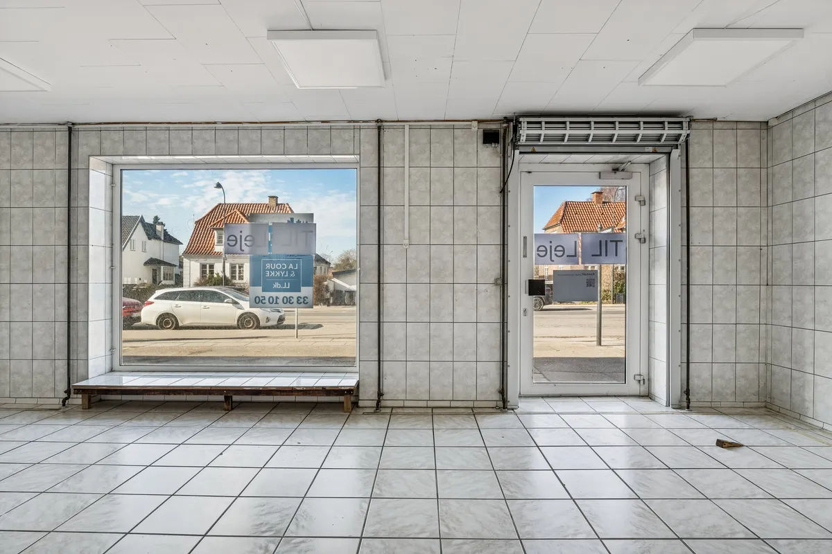 Lejemål i Gentofte med tilhørende parkeringsplads og adgangsdør til en butik med store vinduer.