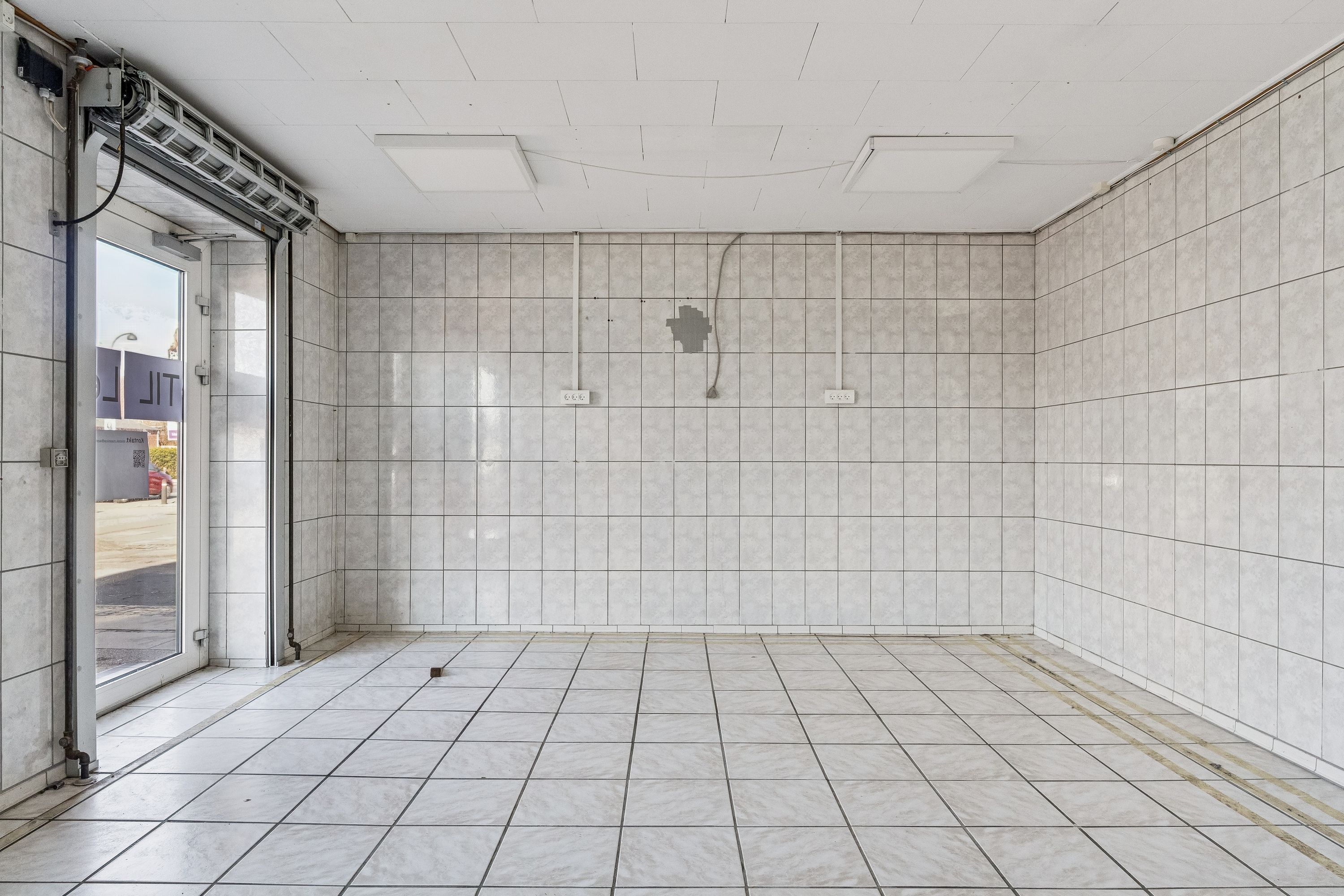 En tom lejlighed med hvide vægge og gulv samt en glasdør og et skråloft med to indbygget lys.