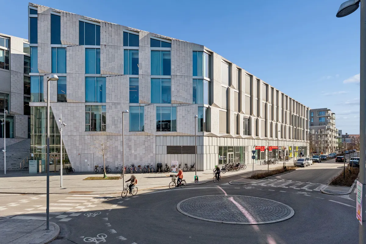 Udlejet erhvervslejlighed i Frederiksberg. Fire cyklister kører langs en tomt rundkørsel med stier og parkeringspladser.