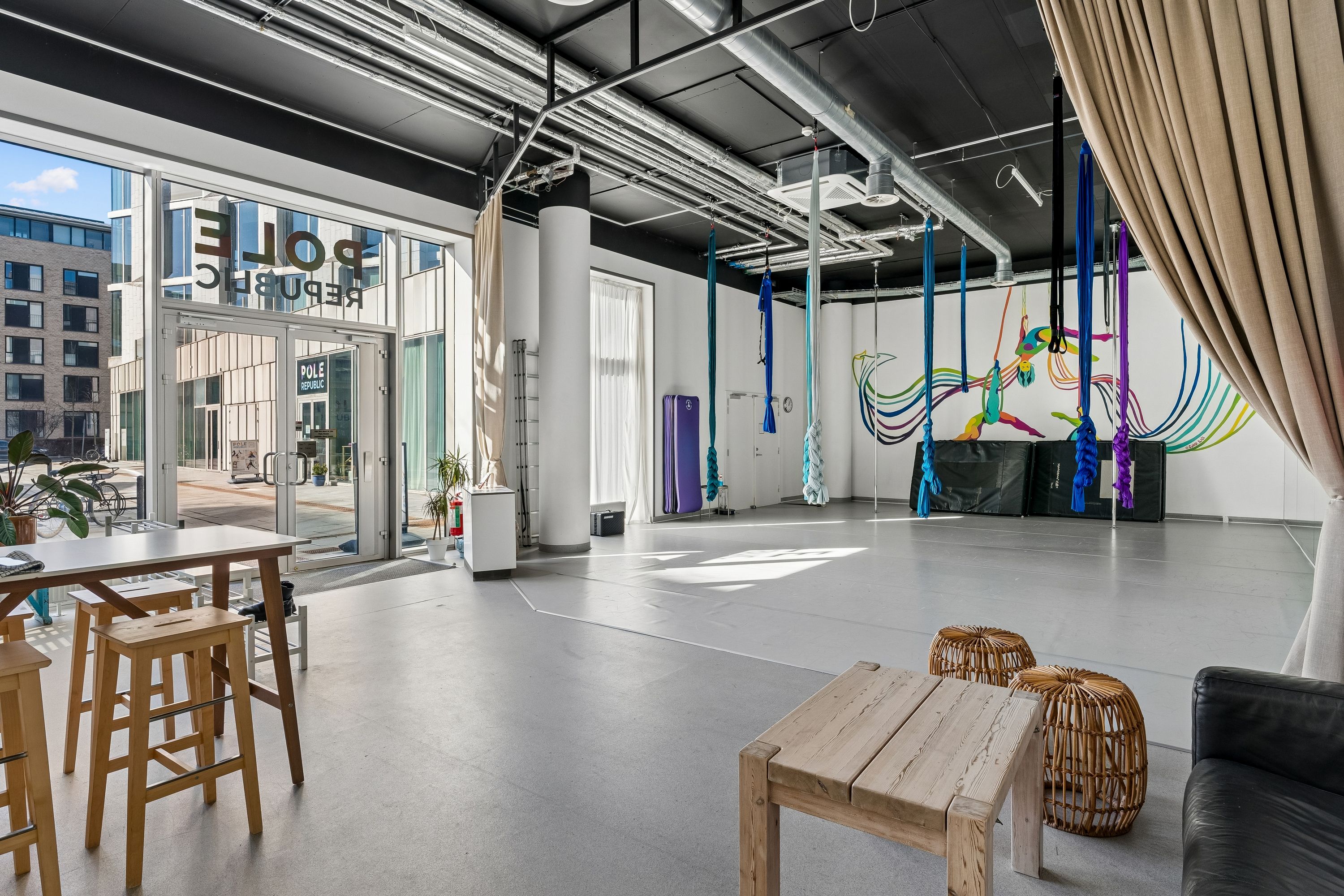 Store lokaler med højt loft, loftsbånd og kunstværk på væggen, træborde og stole, glasdøre, indvendige planter og trægulve