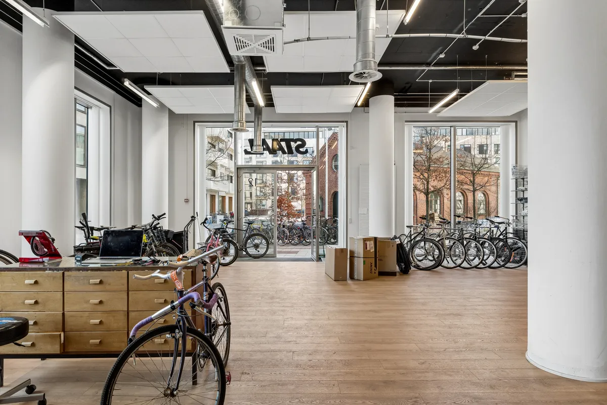 Store, lyse lokaler med moderne indretning, flere cykler stillet op og en skrivebord med laptop. Store vinduer og lyse loftsområder.