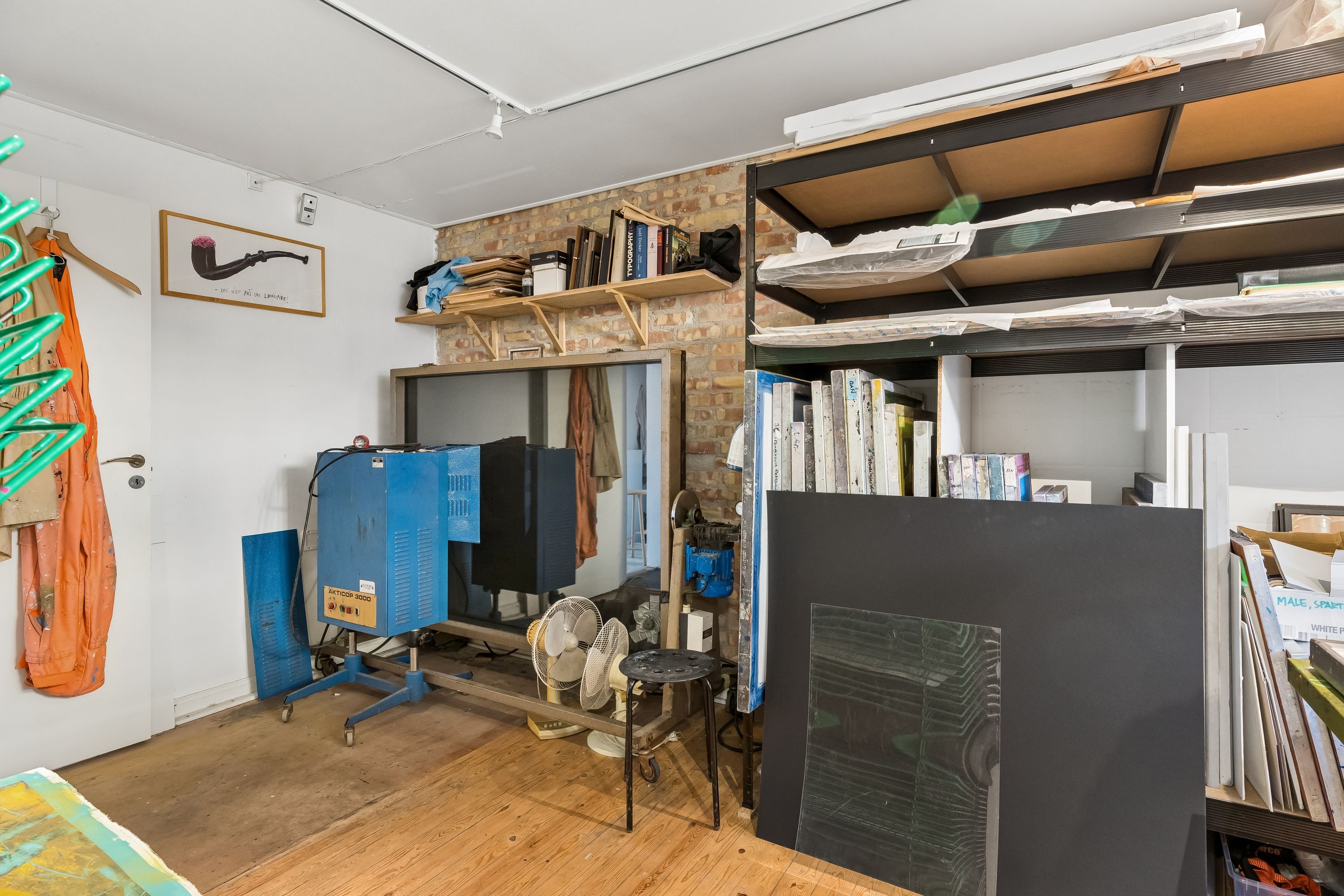 Kunstværkstativ, værktøj og støvler i værksted med loftslampe og hylder med papir og bøger i baggrunden