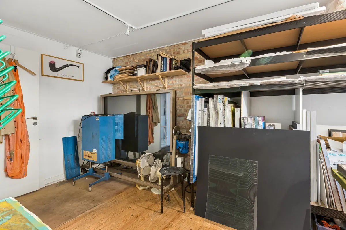 Kunstværkstativ, værktøj og støvler i værksted med loftslampe og hylder med papir og bøger i baggrunden