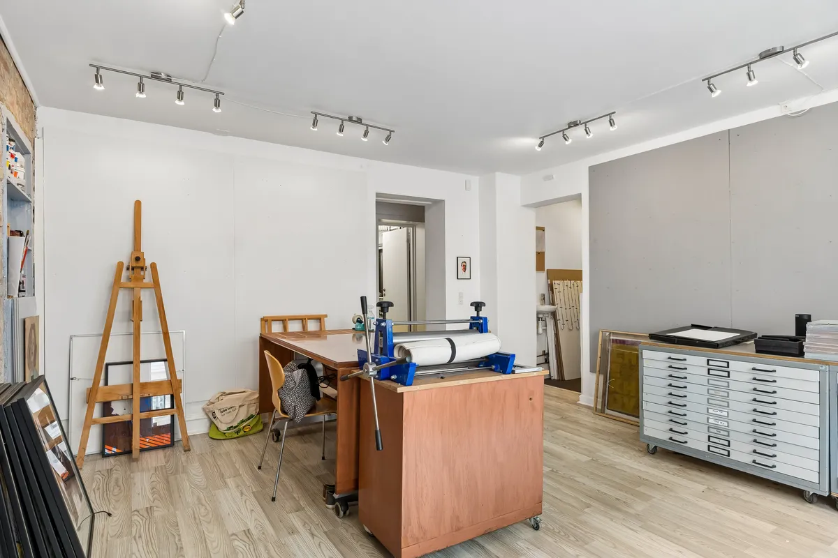 Foto af et højloftet lokale med trægulv, hjørnebord og vinduesåbninger. Væggene er hvide og lyse, og der er højteknologisk udstyr samt kunstværker i lokalet