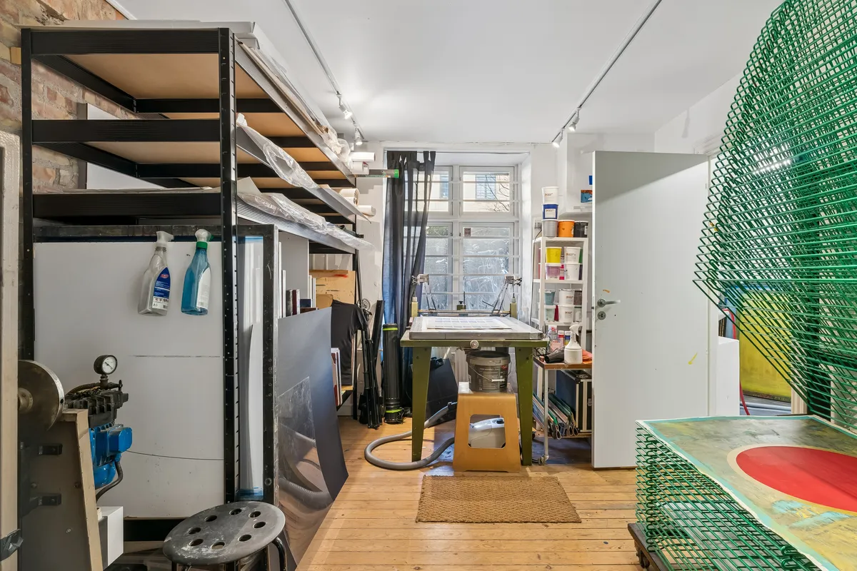 Et værksted med brædder, højrekreds, stol og tømmer. To store grønne net og en større maleri på højrekredsen.