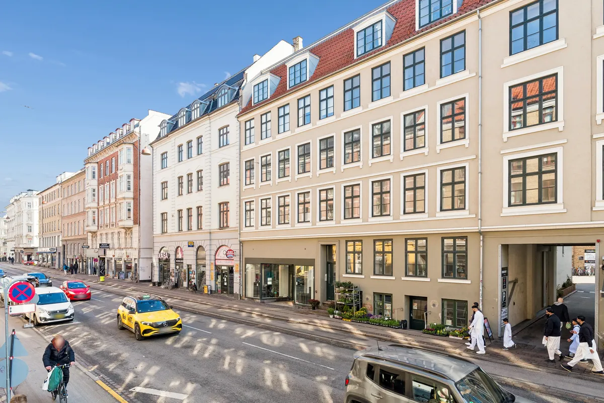 Folk går i gange og kører biler på Vesterbrogade. Her er en butik med blomster, og der er en Mercedes taxi i kørsel. Folk går på fortovet og er iført traditionelle klæder.