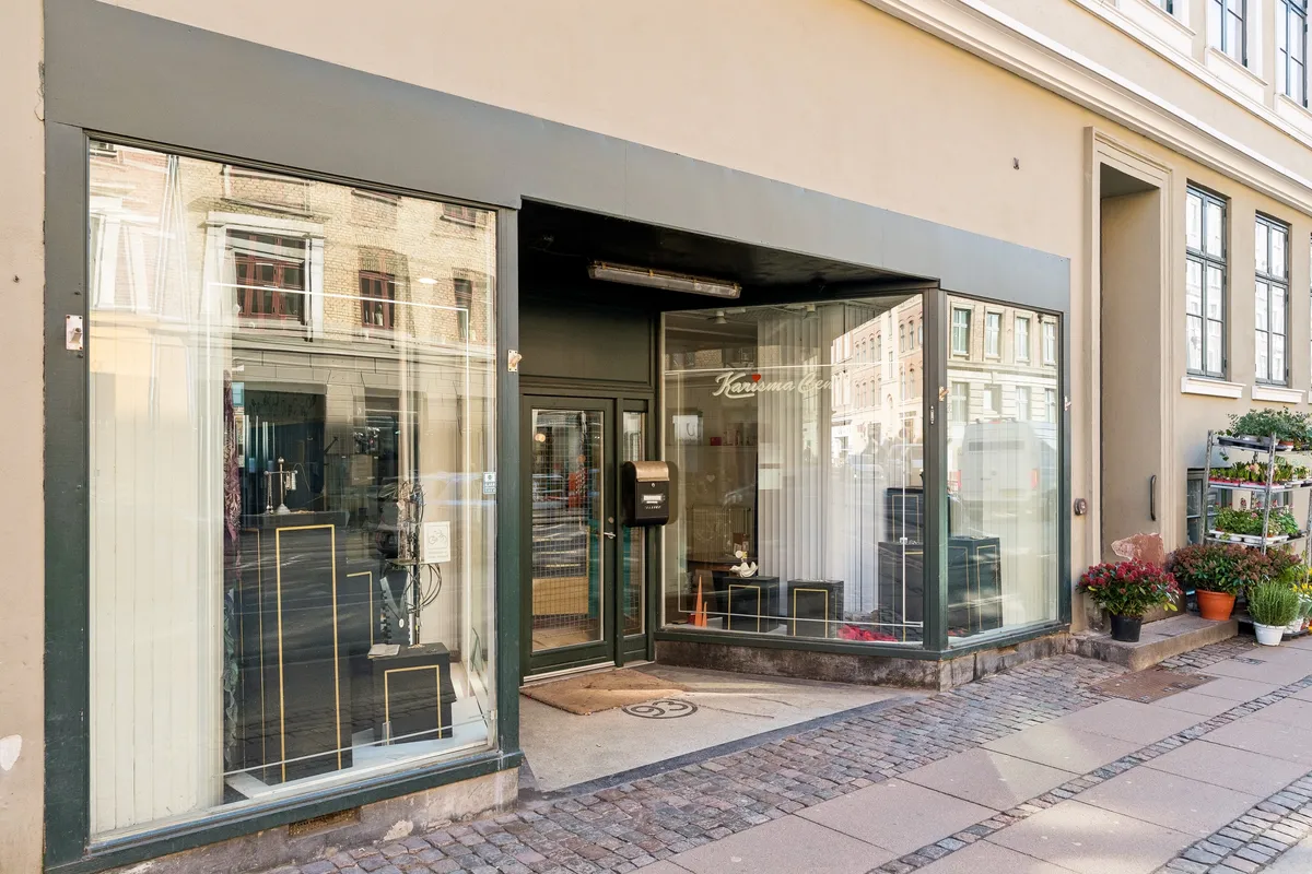 En lejet butik på Vesterbrogade med store glasvinduer og udsmykning med planter og blomster udenfor. Indersiden er møbleret med hylder og ting.