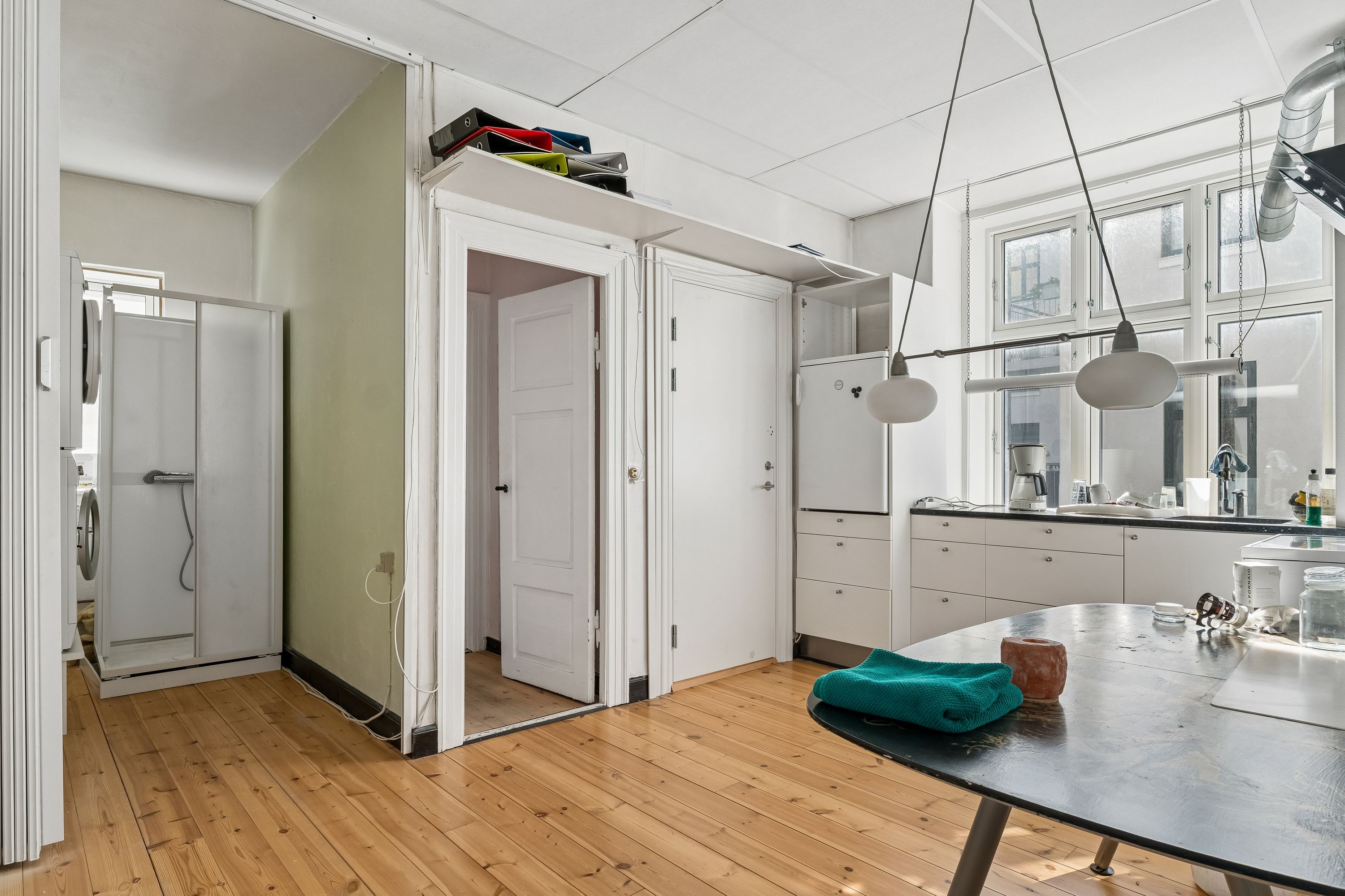 Foto af en moderne køkken med lyse loftslamper, massivt trægulv, en stor rund bord og køkkenudstyret som kaffemaskine, gryder og skarpe glas.