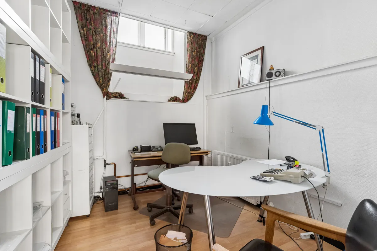 Kontor med skrivebord, computer og møbler samt hylder med papirer og mapper