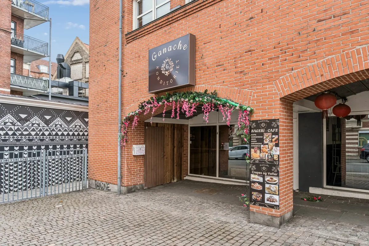 Bageri café med navnet Ganaché Konditorei placeret i røde mursten med dekorationer og blomster i indgangsområdet, og der er flere spisesteder med menukort