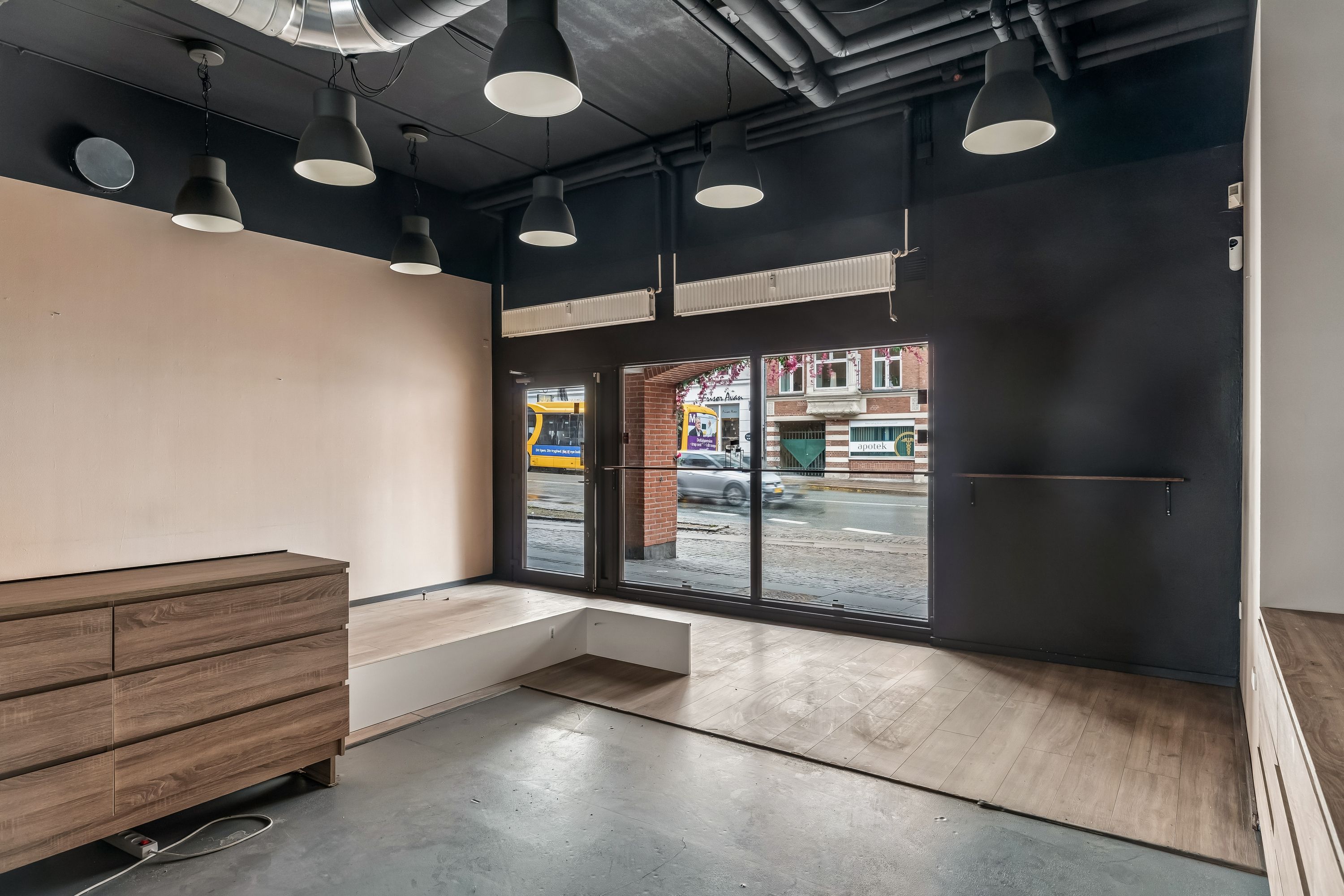 Moderne stue til leje i Valby med store ruder og lyse loftslampe, der skaber et åbent rum med udsigt til Toftegårds Allé og busstation.