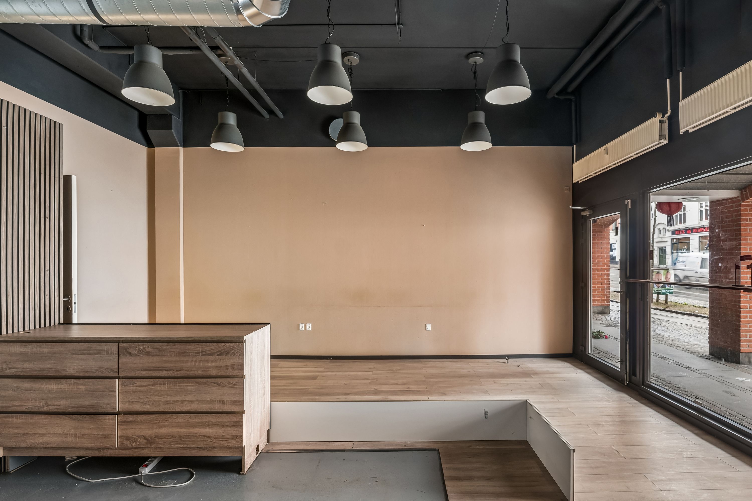 Moderne tomt rum med højloft, lyse og trægulv, lysekroner og møbler i et lejlighedslokal i Valby med udgang til gaden