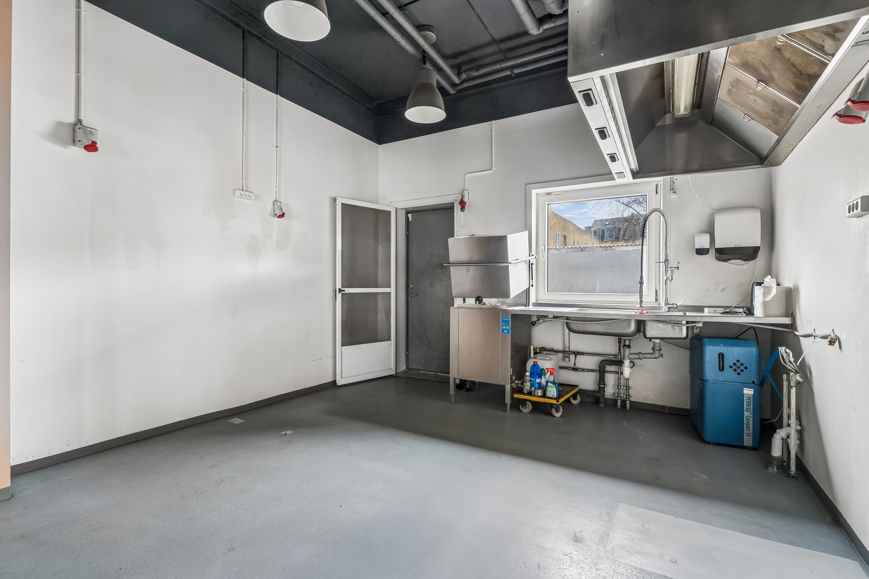 Lejlighed med rå og moderne indretning. Der er et køleskab, 2 senge, et vindue og et køkken med 2 vandhaner og en skraldkurv.