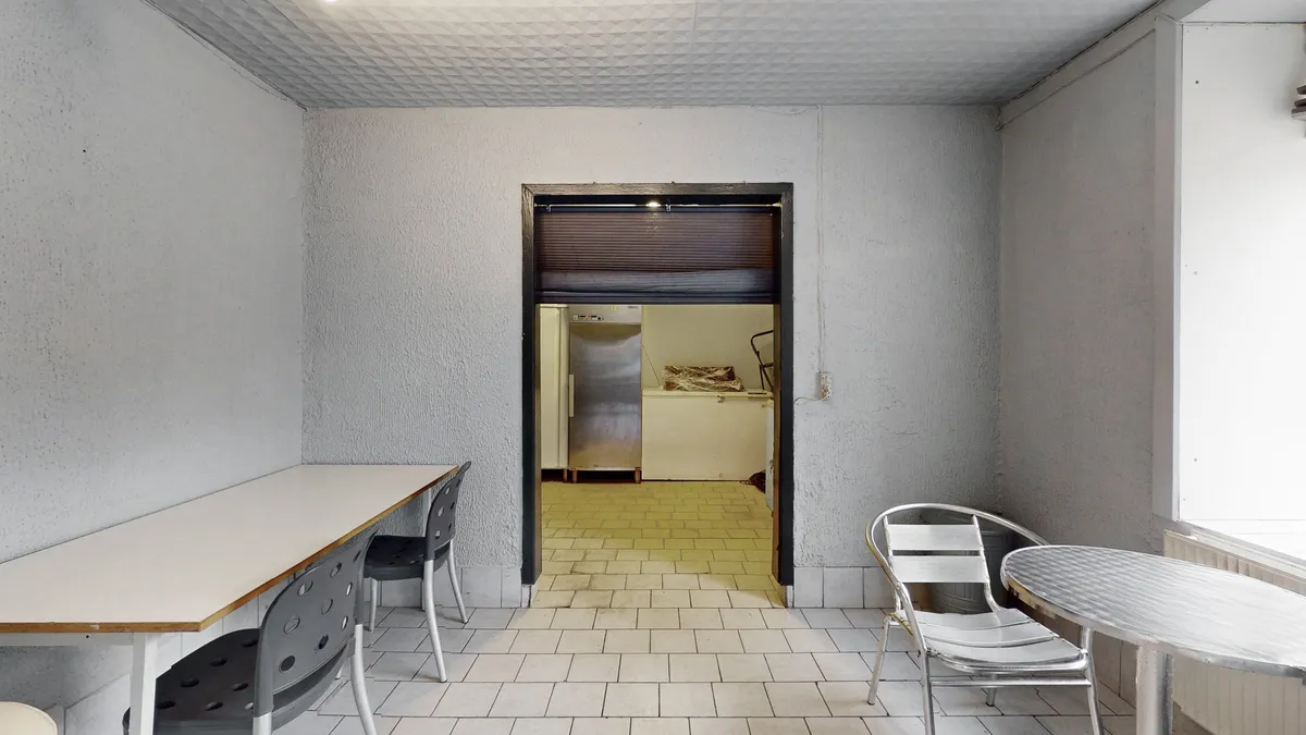 Køkken med lysegule fliser, to stole ved bord, køleskab og loftslampe, en åben dør og et gulv med mønstre