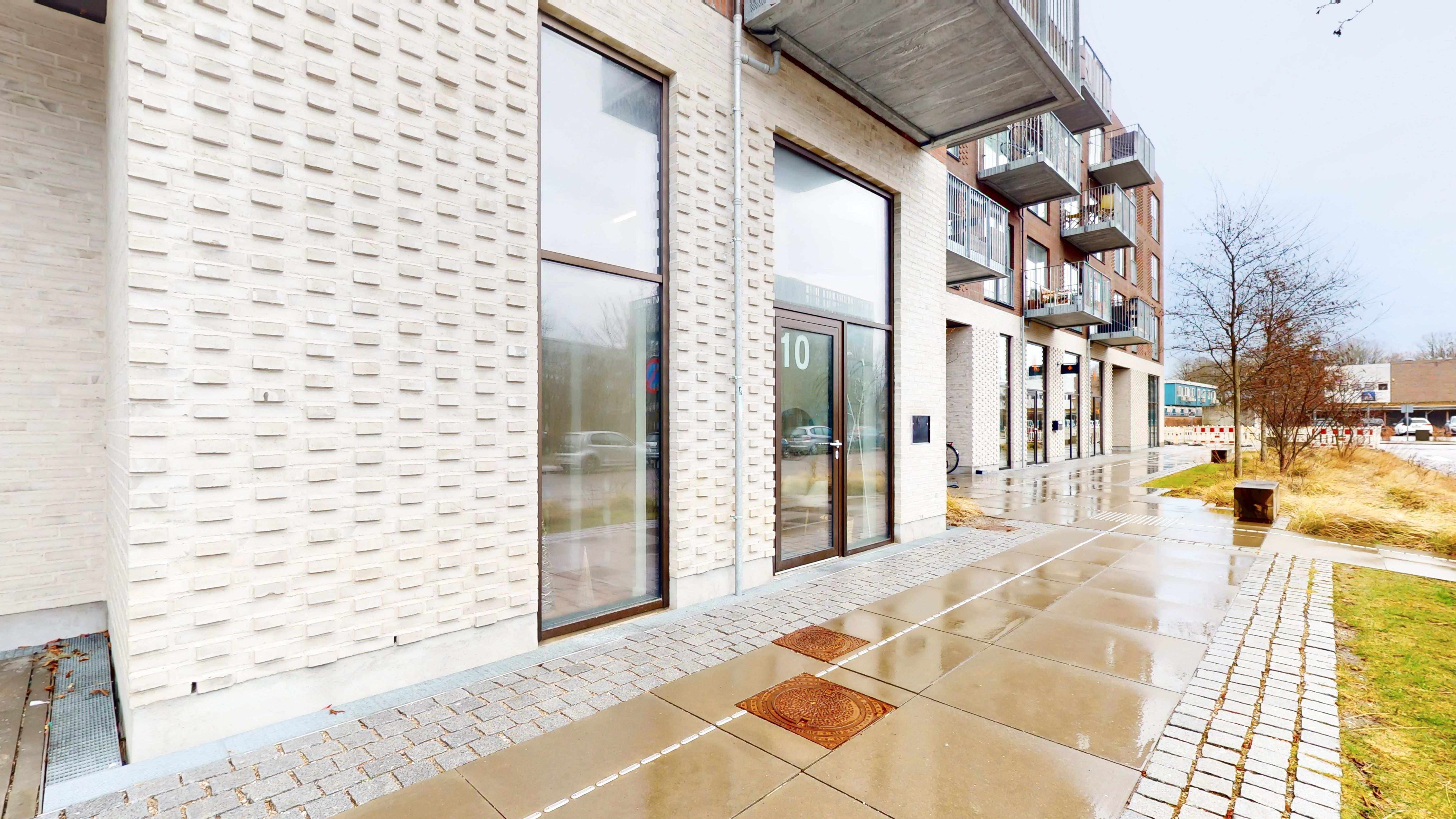 Et erhvervslejemål med store glasruder og en stor nummerplade, der læser 10, med grønne vejspærringer og skrånende vejside.