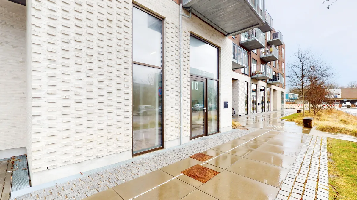 Et erhvervslejemål med store glasruder og en stor nummerplade, der læser 10, med grønne vejspærringer og skrånende vejside.