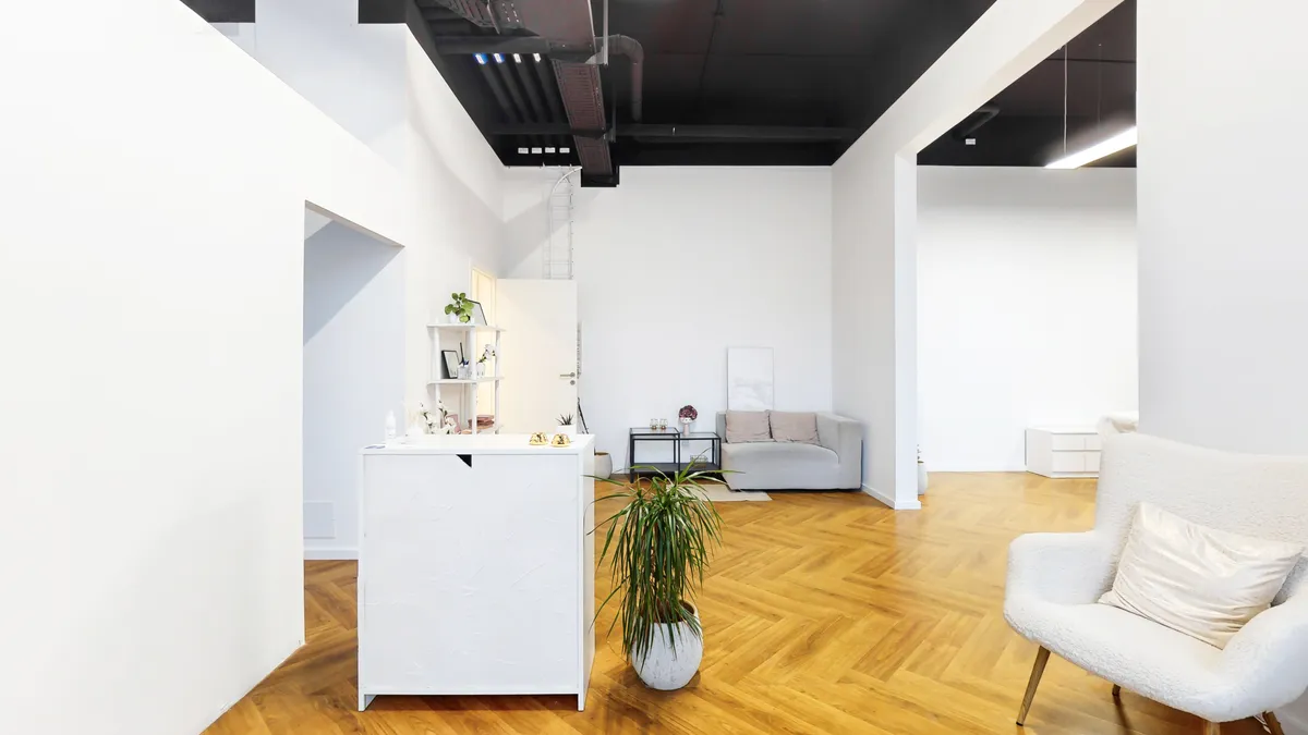 Kontor med højt loft, moderne møbler, gul gulv og indretning med hvide vægge, sofa, bord og bokse. Et hvidt bord med plante og flere objekter.