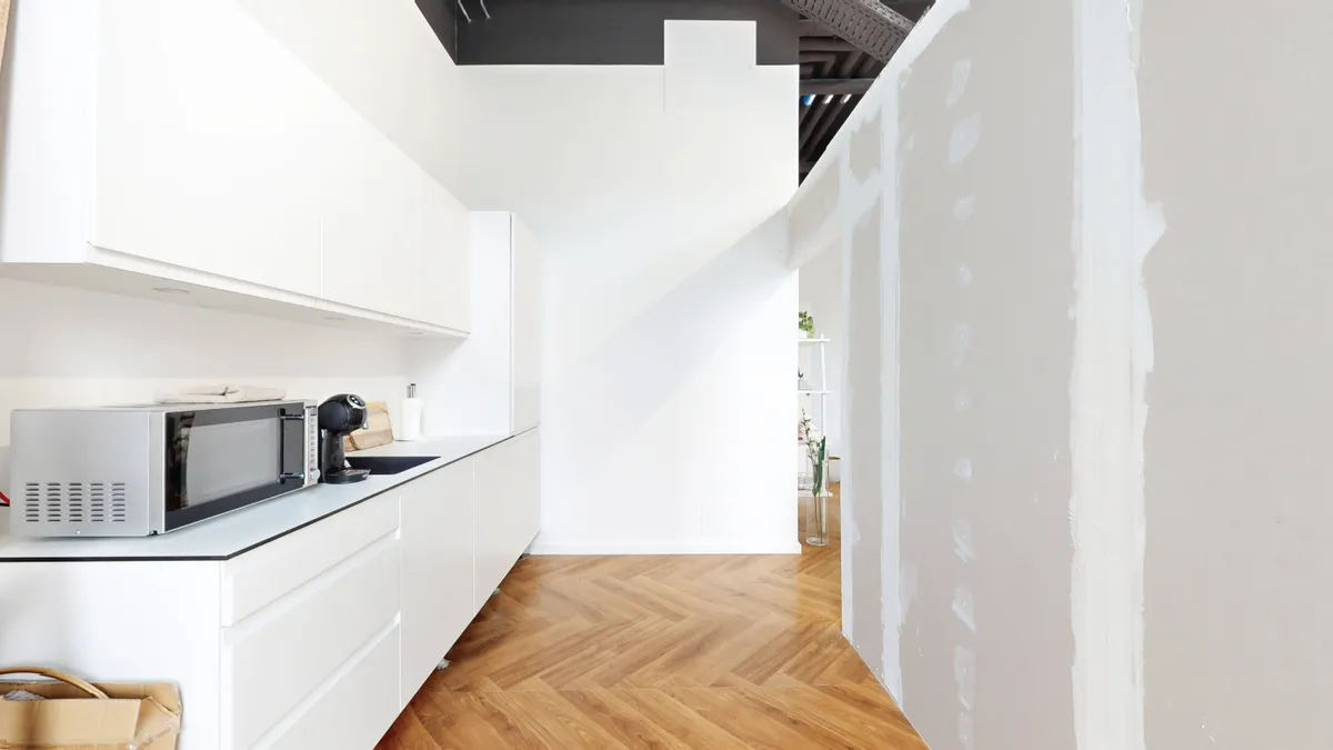 Et minimalistisk køkken med hvide vægge og loft og et køkken med hvide kabinetter og en mikrobølgeovn.