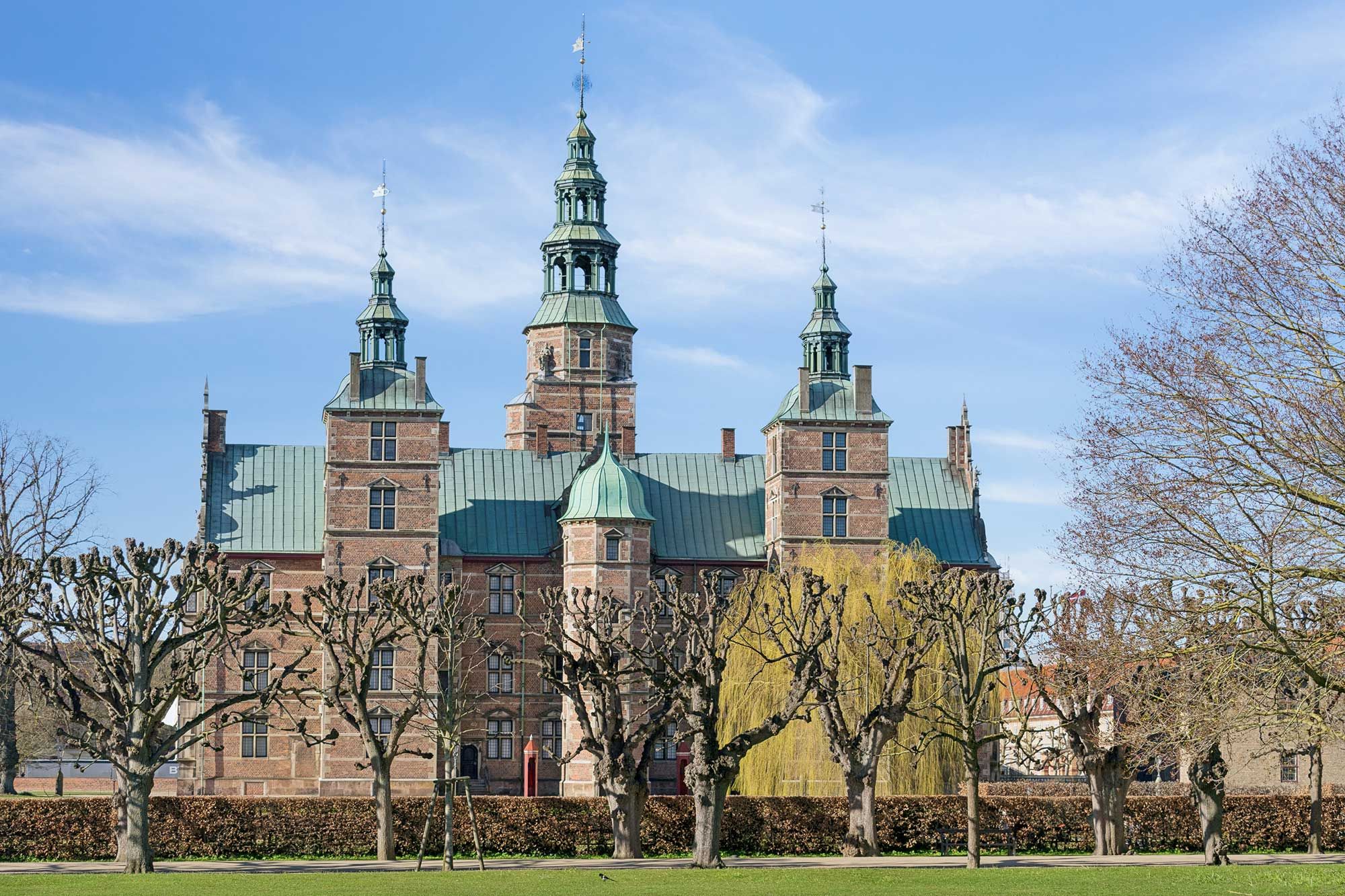 Københavns Slotsholmen med tre tårne og smukke træer foran lyseblå himmel med skyer