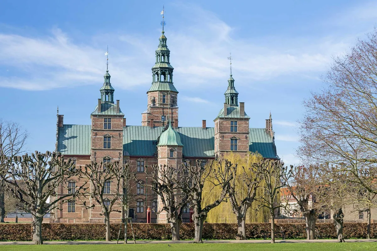 Københavns Slotsholmen med tre tårne og smukke træer foran lyseblå himmel med skyer