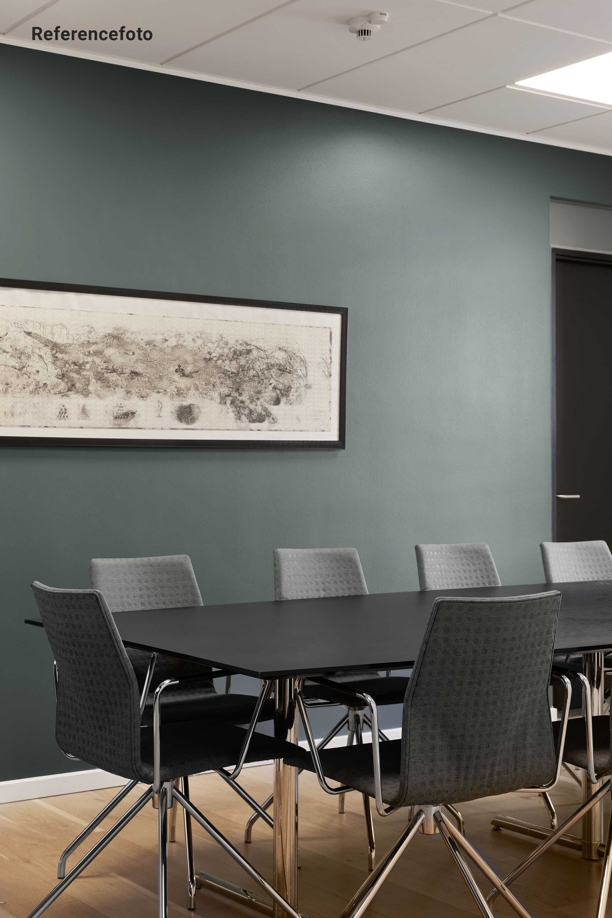 Kontormøbler med høje stolben og tynd metalramme. Bord med høje ben og slank kant. Væg i lyseblå og ramme om kunstværk. Hvid loftsbeklædning og gul trægulv.