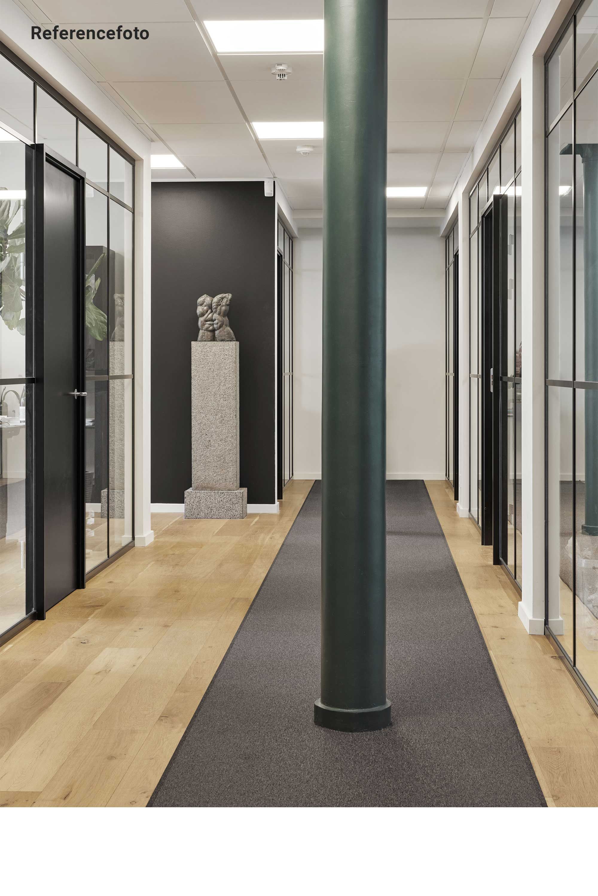 Et kontorlokal med lyse lofter og store glasvinduer er i gang med istandsættelse. Væggene er mørke og der er en skulptur på en sokkel i enden af gangen