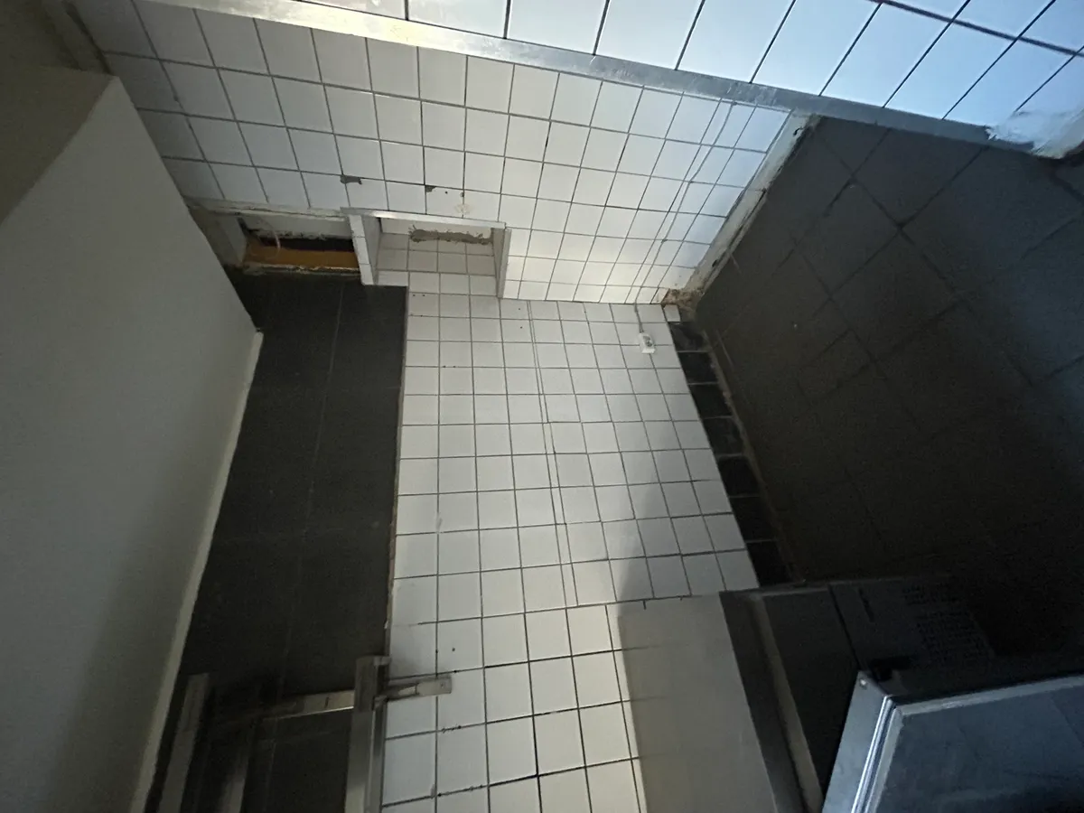 Take-away til leje på Nordre Frihavnsgade 55, 2100 København Ø. Rummet med hvide og sorte fliser og et køleskab. Hjørner med skrald og en gul bjælke.