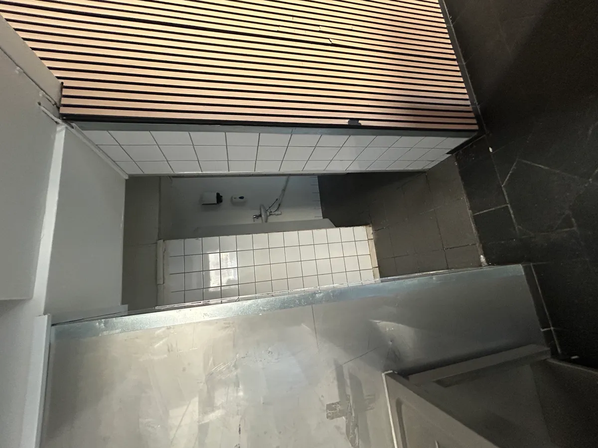 Forretningslokale til leje med udsugning. Lokale med gulv og hvide tøjbrætter samt metaldør og møbler