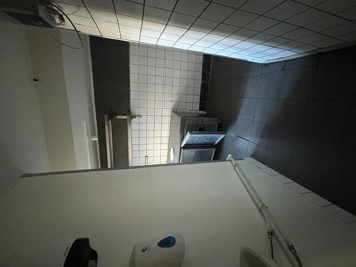 Toilet med hånddesinficering og flere håndklæder i en højre sidevæg med hvide fliser og mørke gulvfliser