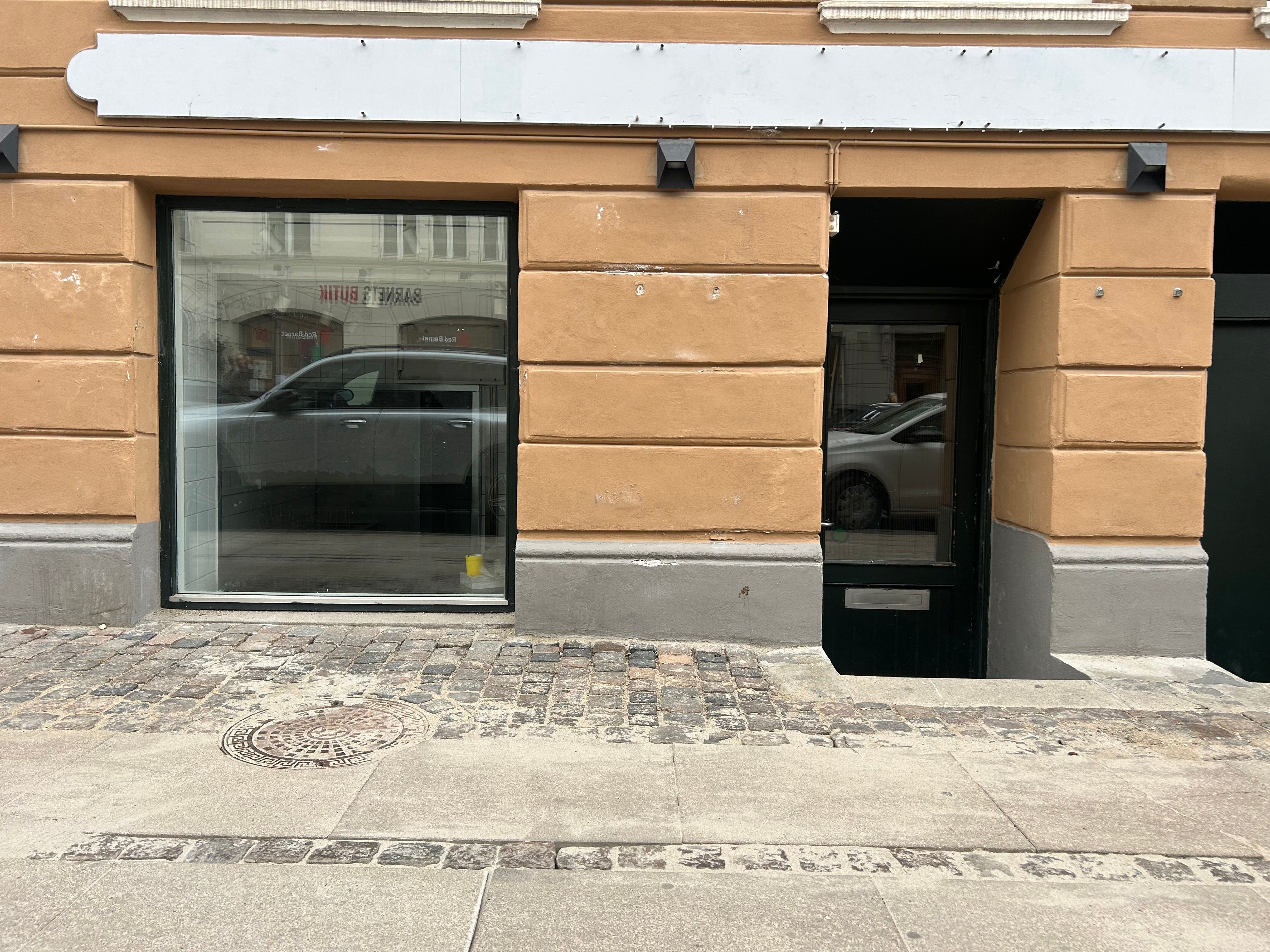 Take-away med glasvinduer, gulv og vægge med lyse farver, udstyret med belysning. Bygningen med lysegul facade og mørke vinduer. Lysrefleksion i glasvinduerne.