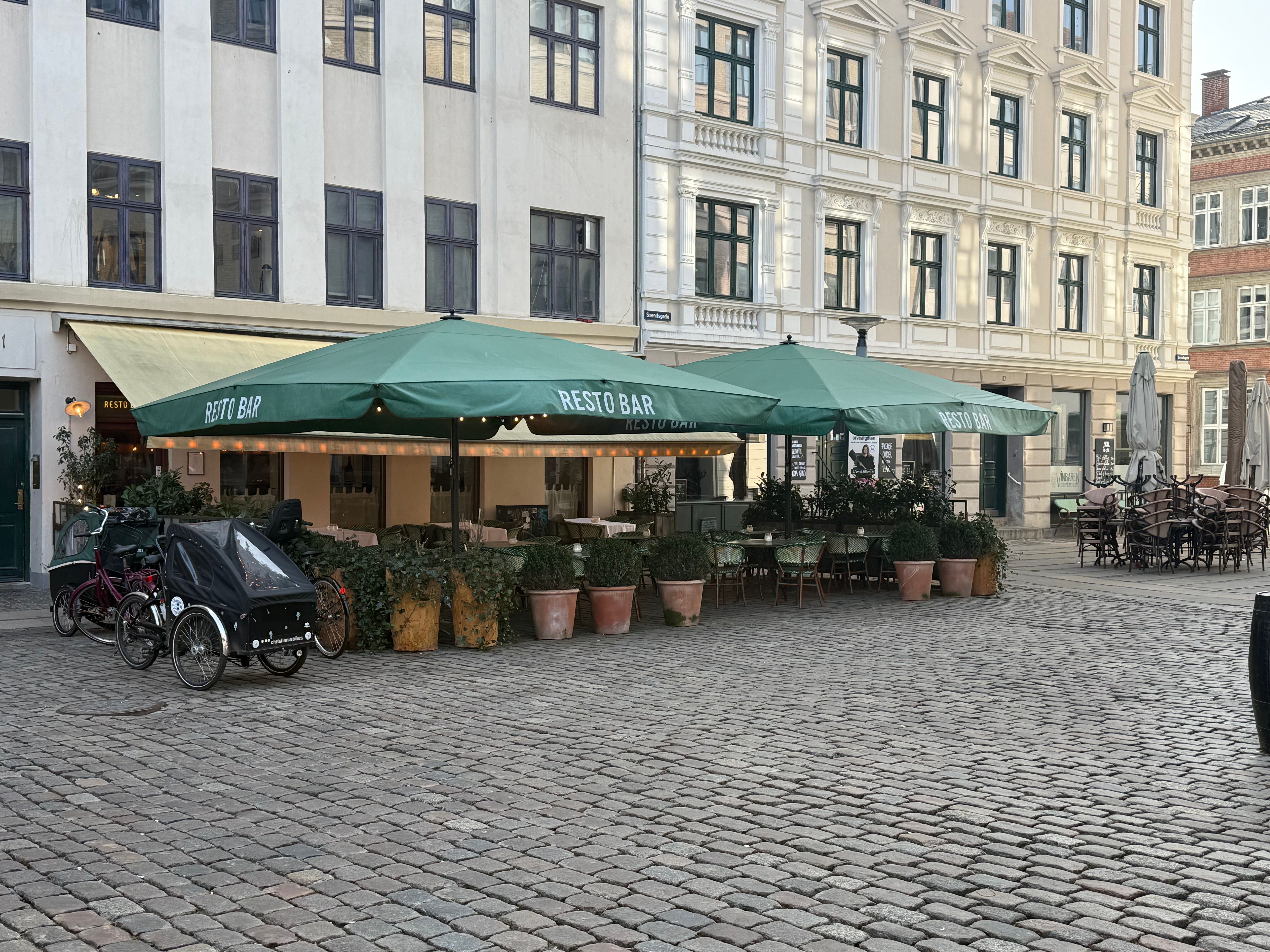 Grønne parasoller og borde med plantager på terrassen foran Resto Bar på Vesterbrogade i København