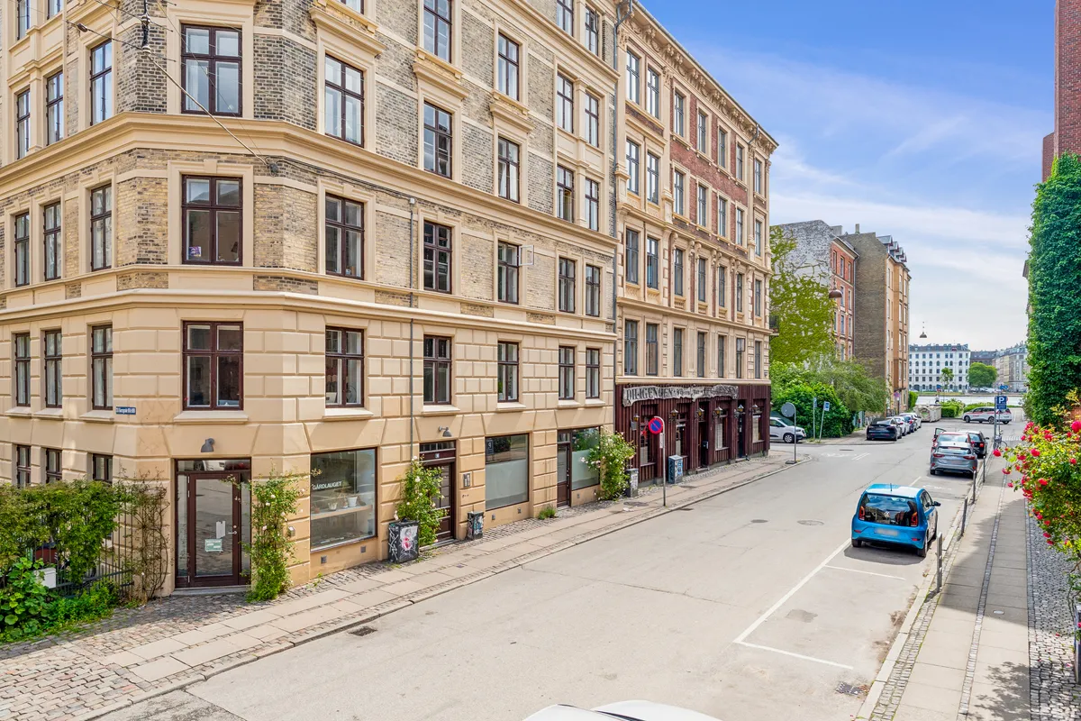 Korsgade i København med en stor bygning, der er udsmykket med mange vinduer og et glasdækket butiksvindue