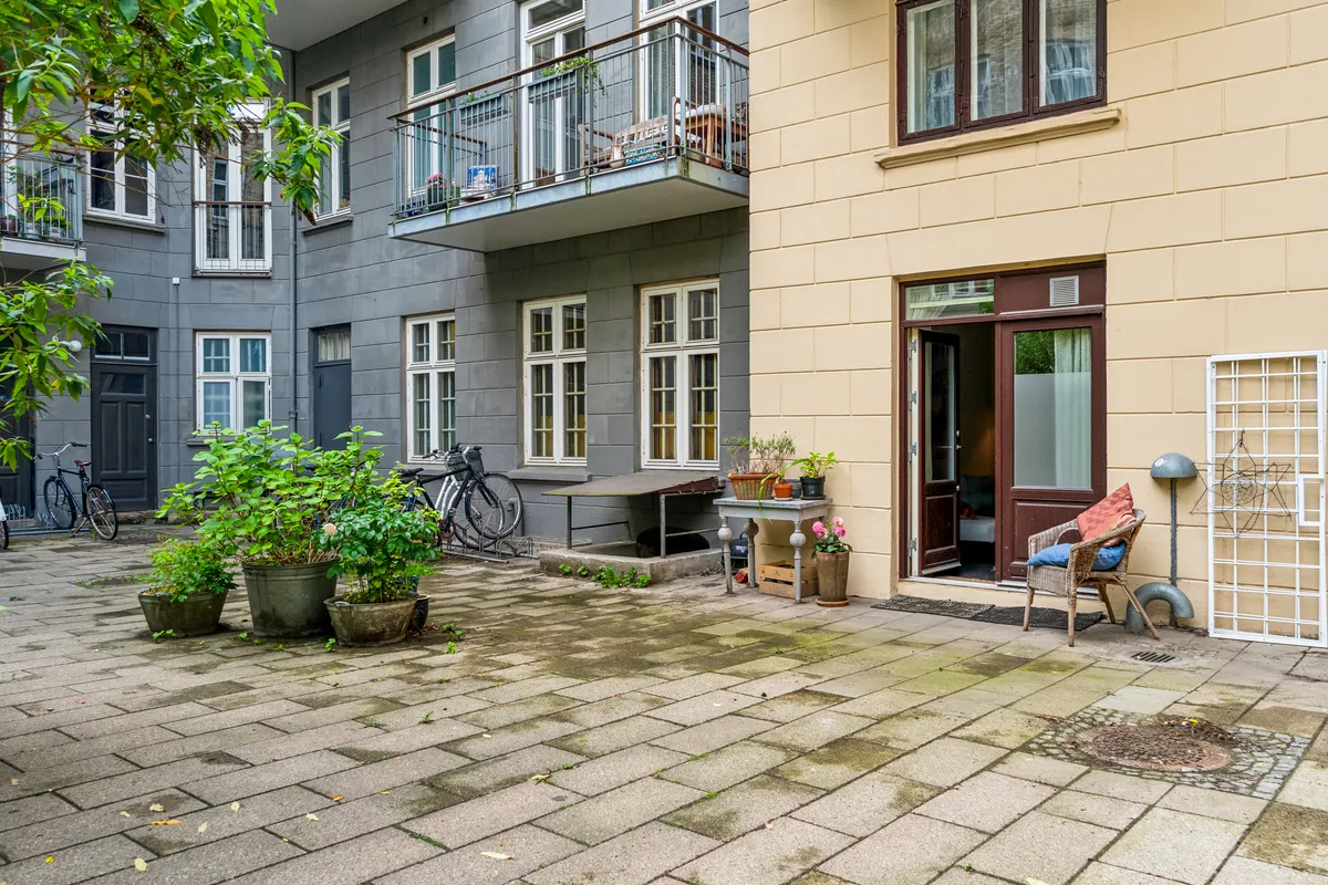 Et smukt gårdhave med terrasse, blomster, grønne planter og en stol med tæppe. To cykler står uden for. Gårdhave til lejligheden Korsgade 10, st. 4, 2200 København N.