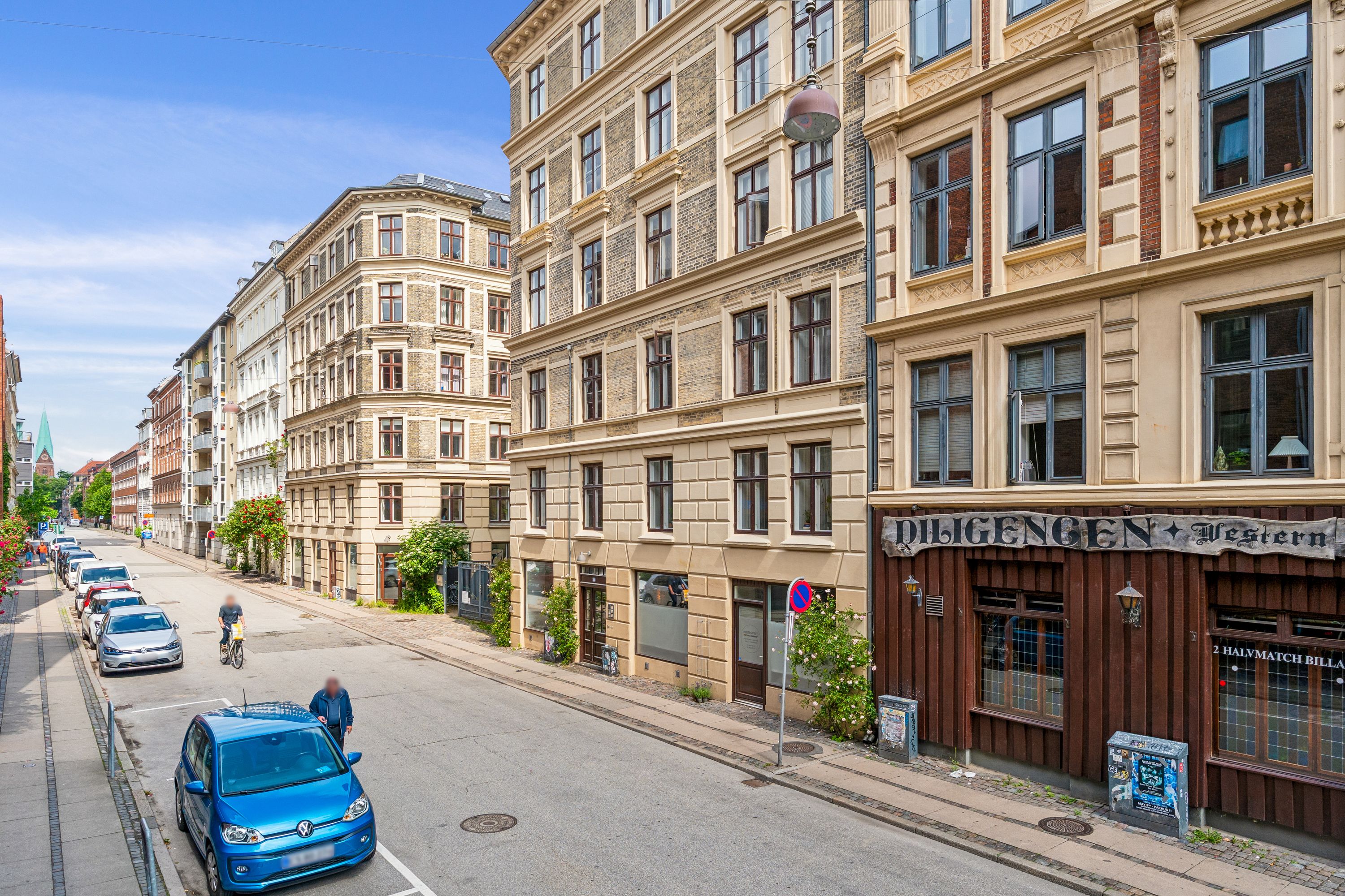 Butik på Korsgade med reklameskilt og gågade med parkerede biler og gående personer