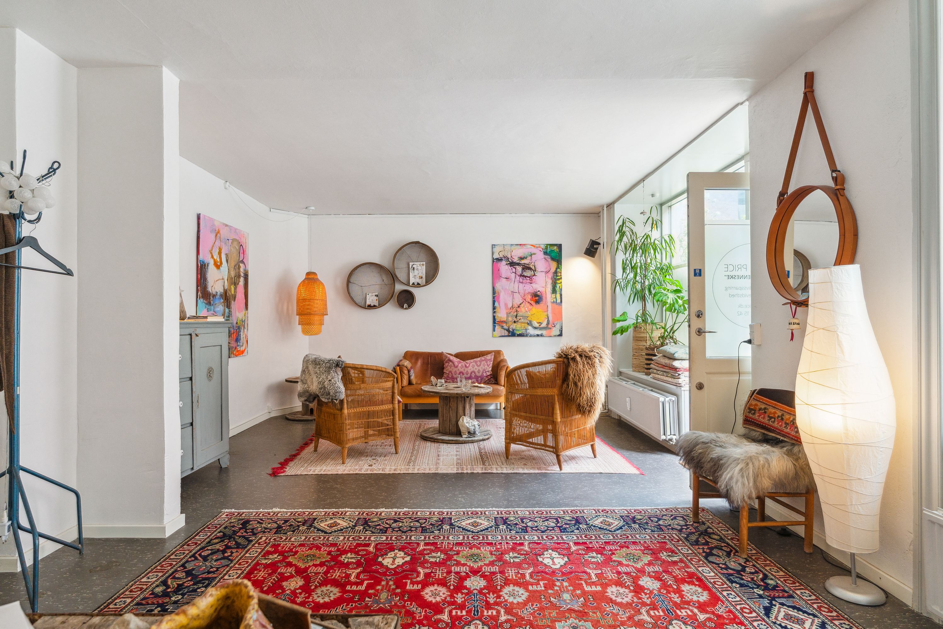 Et stort lyse interiør med højt loft og gulvbelægning af træ. I rummet er der en sofa, stole og tavler på væggen. Midt på gulvet er der to tykke tæpper