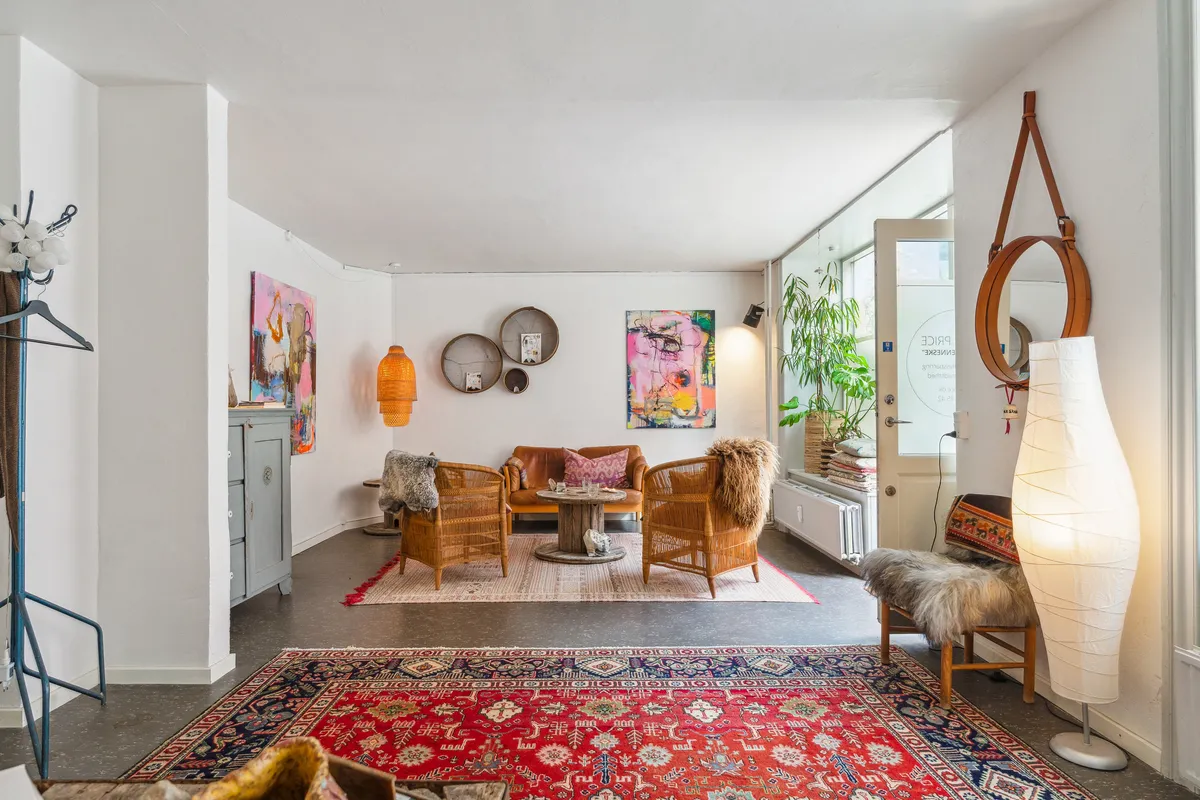 Et stort lyse interiør med højt loft og gulvbelægning af træ. I rummet er der en sofa, stole og tavler på væggen. Midt på gulvet er der to tykke tæpper