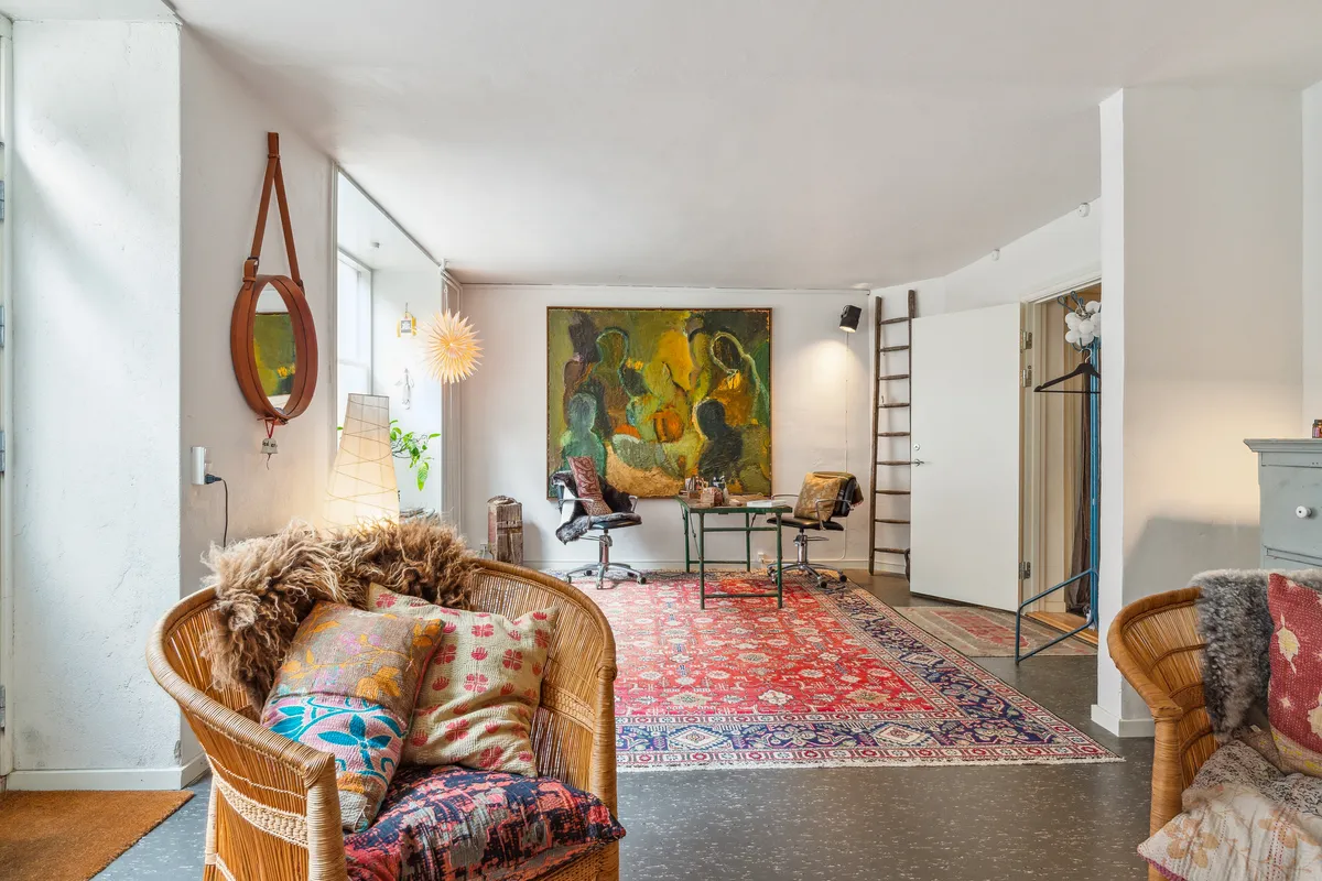 Køkken med stol, bord og kunstværk på væggen samt tæppe på gulvet og stole med tæpper og puder