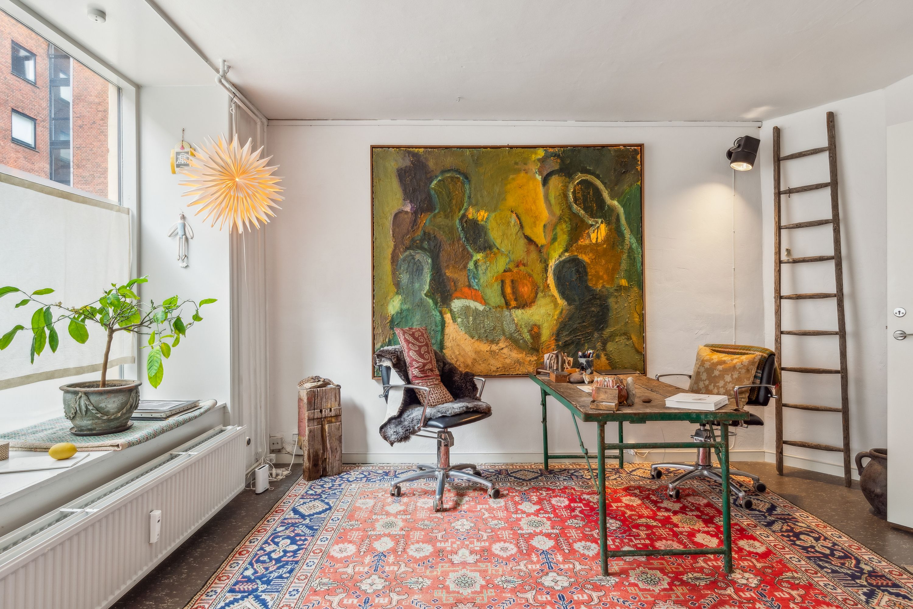 Københavnsk lejlighed med rummeligt arbejdsrum, stort kunstværk, skrivebord, stole, plante, højt vinduesparti, gulvtæppe og lysekroner
