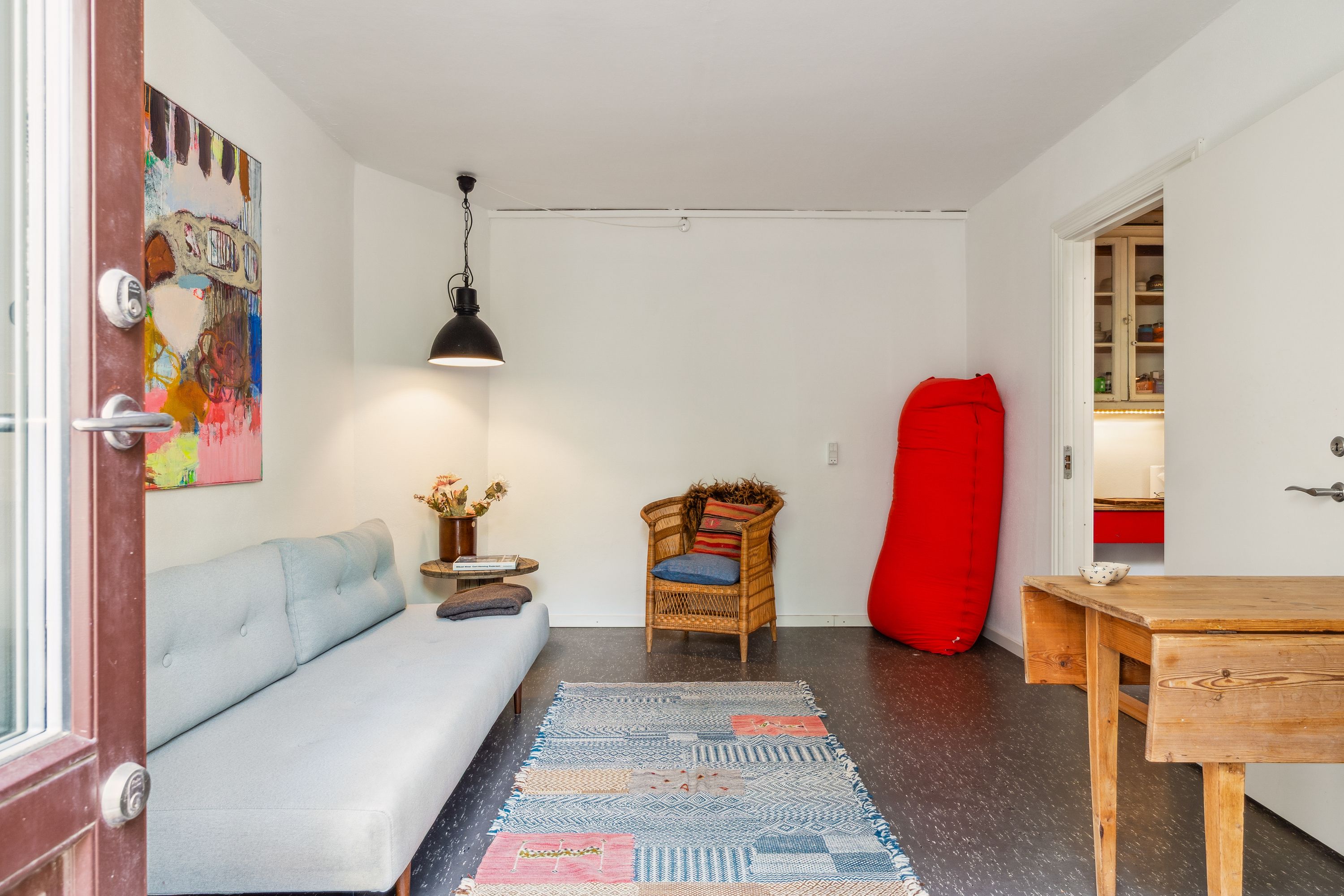 Køkken med lysegul væg og møbel med lyseblå pudsede sofa, stol med tæppe og rød pude, træbord med skål og blomster i vase