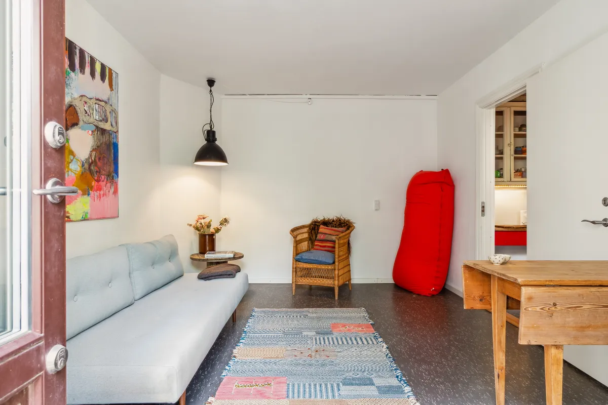 Køkken med lysegul væg og møbel med lyseblå pudsede sofa, stol med tæppe og rød pude, træbord med skål og blomster i vase