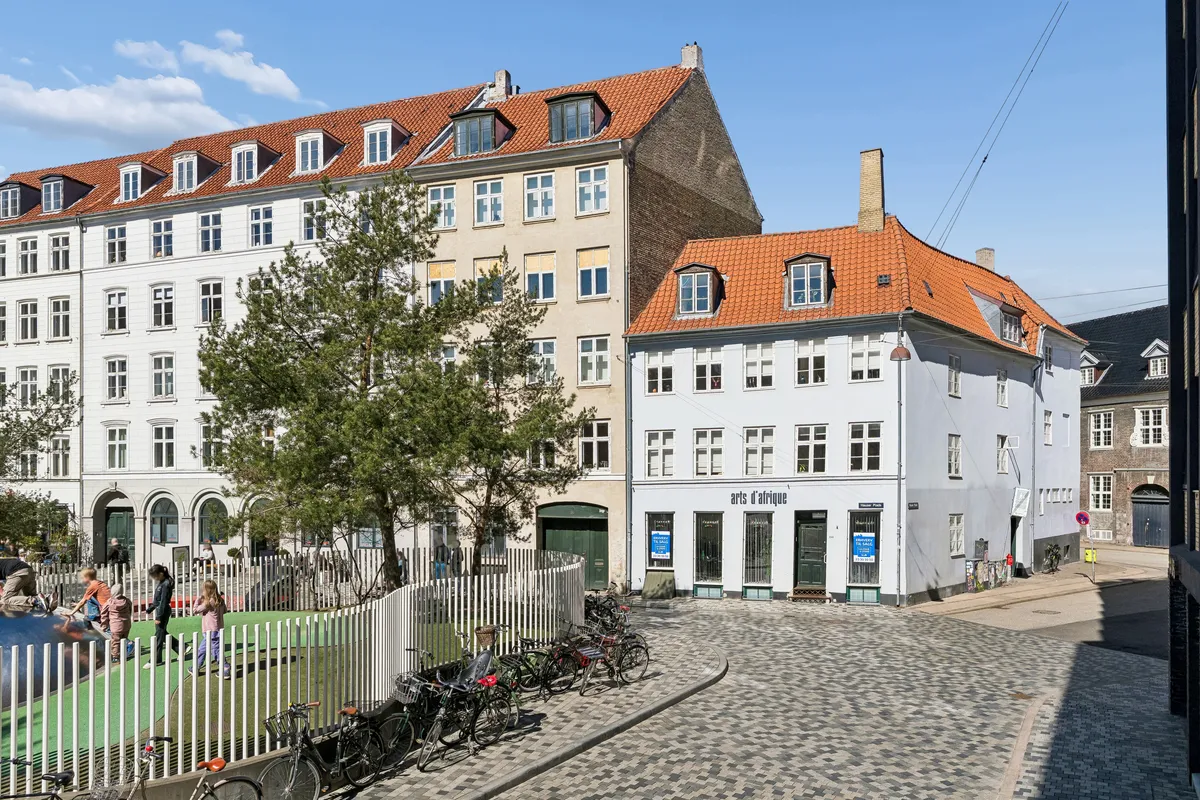 Park med grønt græs, børn, kvinder og mænd, cykler, huse, røde tag, hvide vægge, røde tage, røde tag, hvide ruder, røde tage, hvide ruder, røde tage, hvide ruder, røde tage, hvide ruder, røde tage, hvide ruder