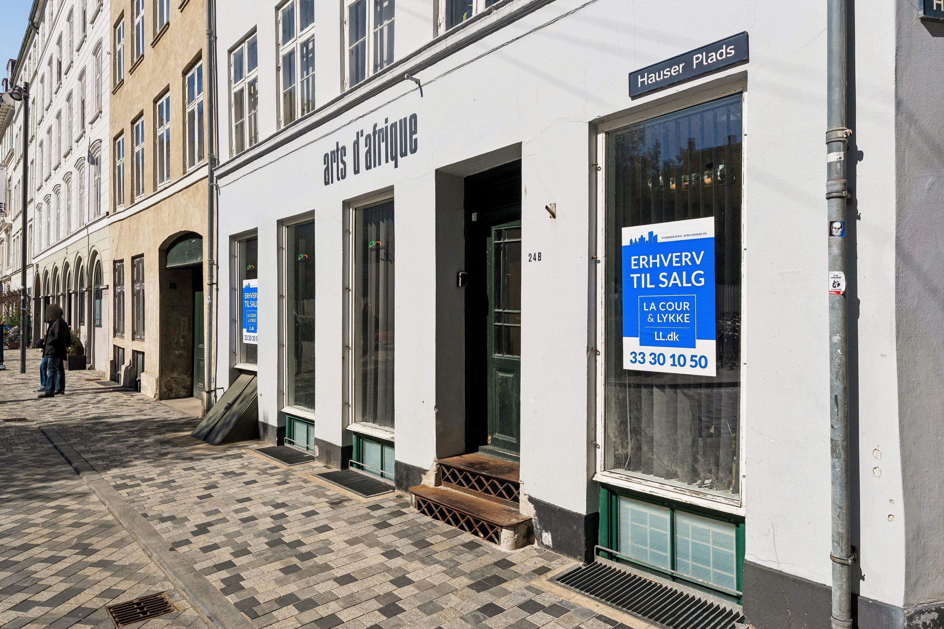 Kontor til salg på Hauser Plads 24, st., 1127 København K. Bygningen med en facade i hvid og grøn farve. Et skilt med teksten "Erhverv til salg" er opsat i vinduet.