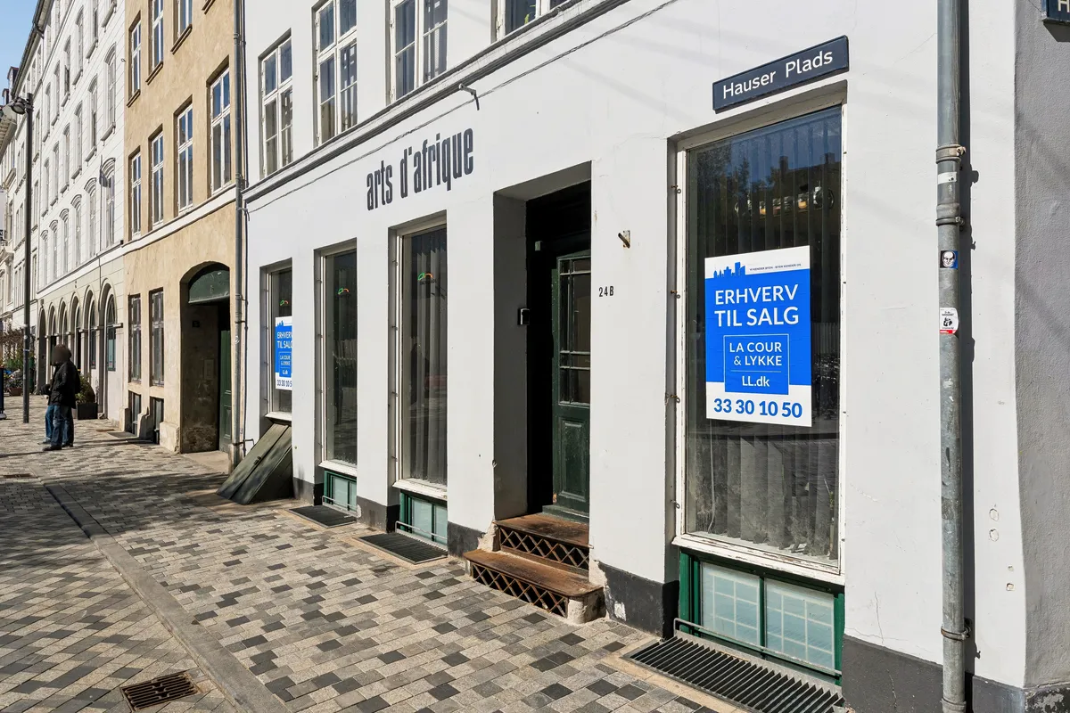 Kontor til salg på Hauser Plads 24, st., 1127 København K. Bygningen med en facade i hvid og grøn farve. Et skilt med teksten "Erhverv til salg" er opsat i vinduet.