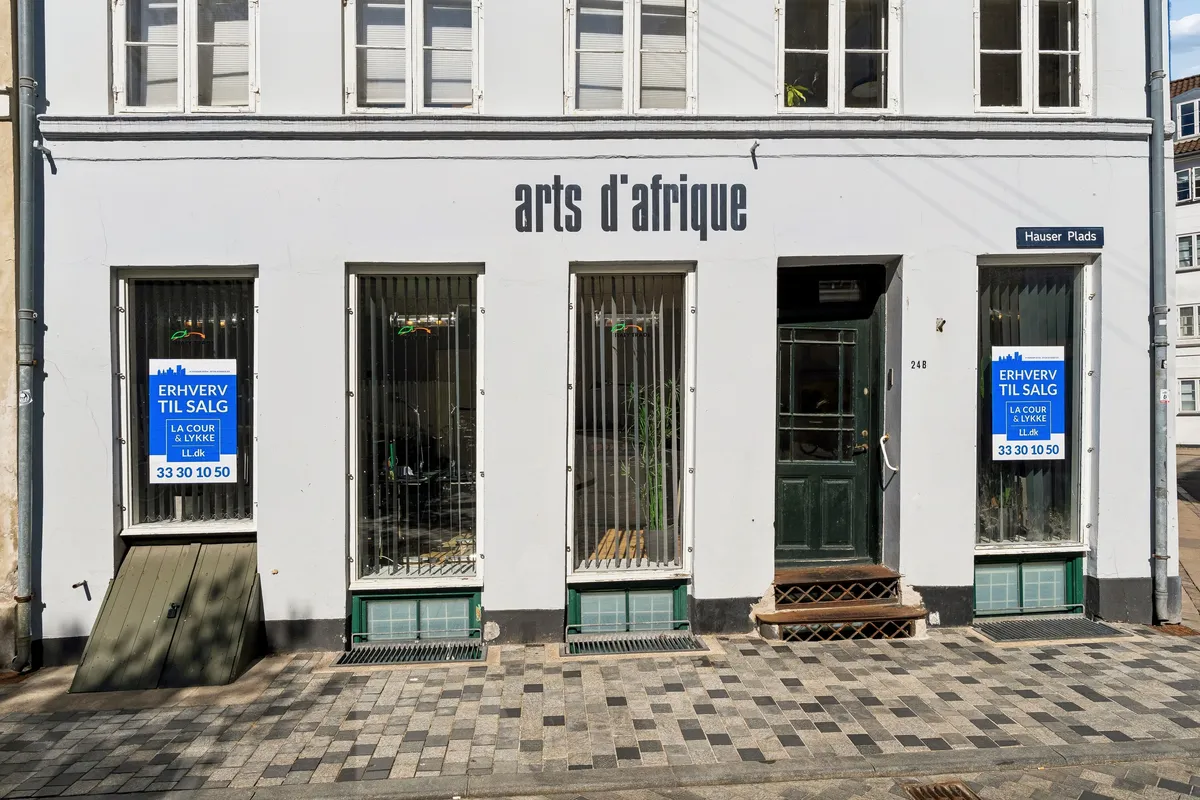 Kontor til salg i 24B Hauser Plads, København. Lukket med gitter og glasruder. Stående skilte med tekst "Arts d'Afrique" og "Erhverv til salg". Adresse skilt læser "Hauser Plads".