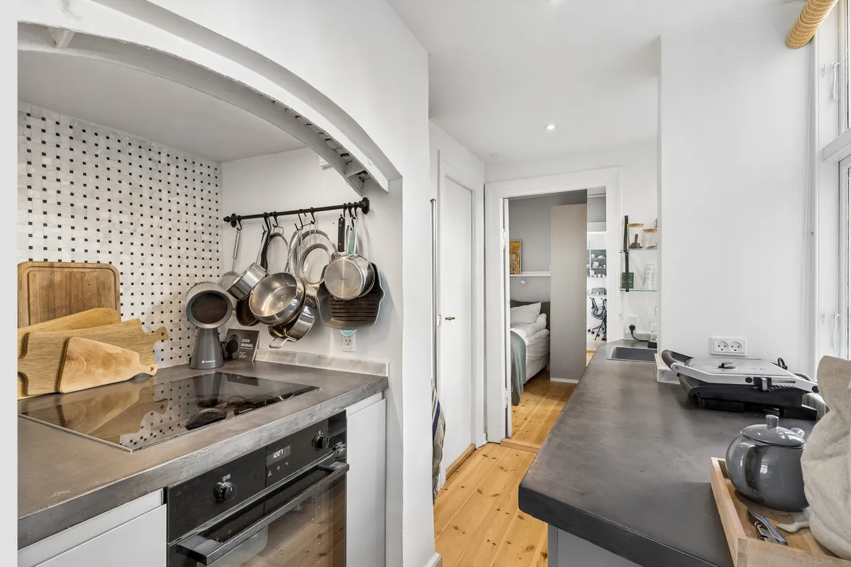 Køkken med hvide vægge og loft, en indbygget ovn, et komfur, og et udstyret køkkenbord med en tepotte og en gryde