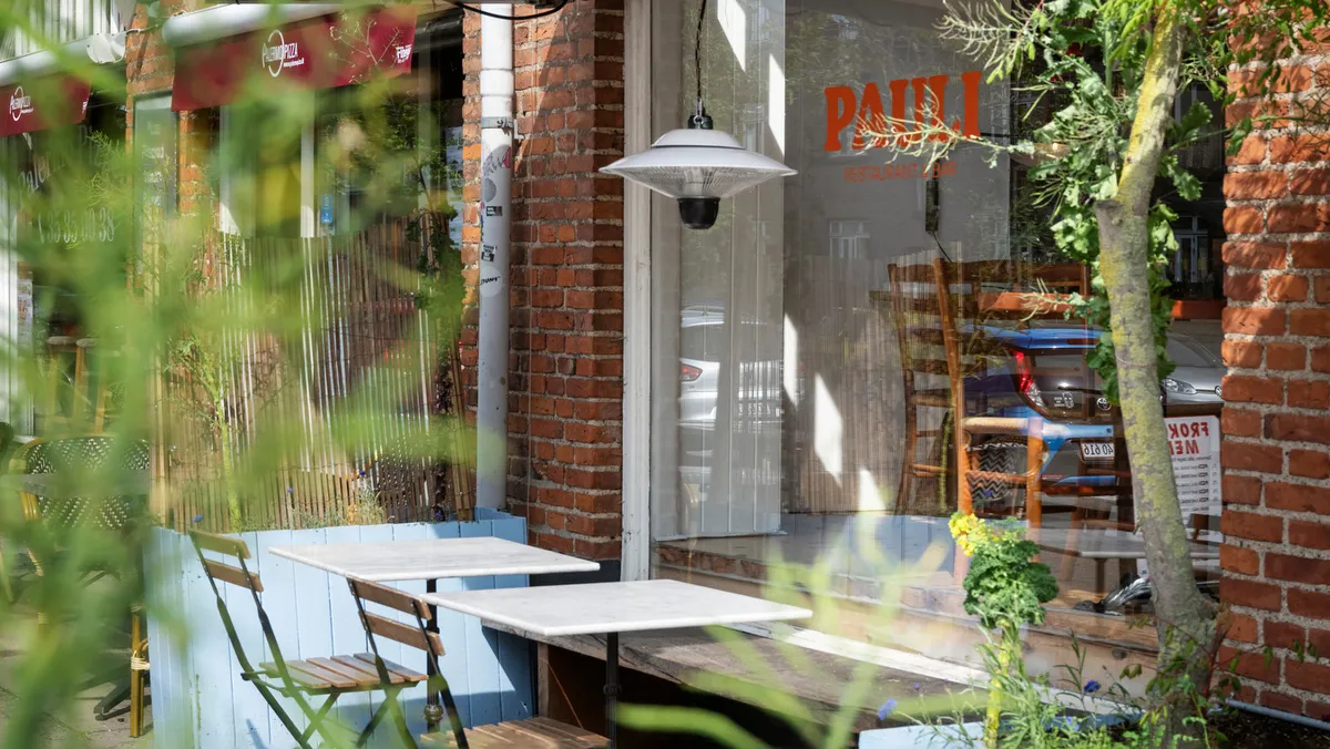 På Borgbjergsvej 13 i København er der en restaurant med lyse møbler og en terrasse med to bord og stole. En pærelampe hænger udenfor, og der er en bord med stole inde i restauranten.